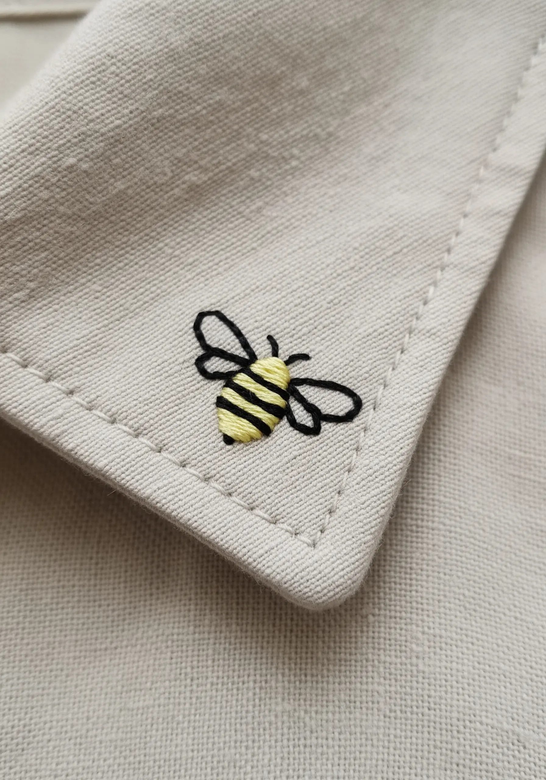 Tiny embroidered bee with yellow and black stripes on a shirt collar.