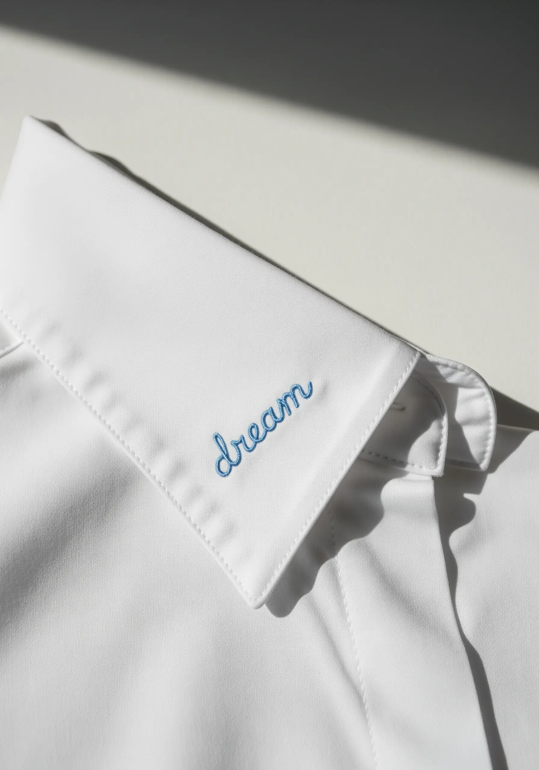 Delicate blue cursive lettering embroidered on the corner of a white shirt collar.