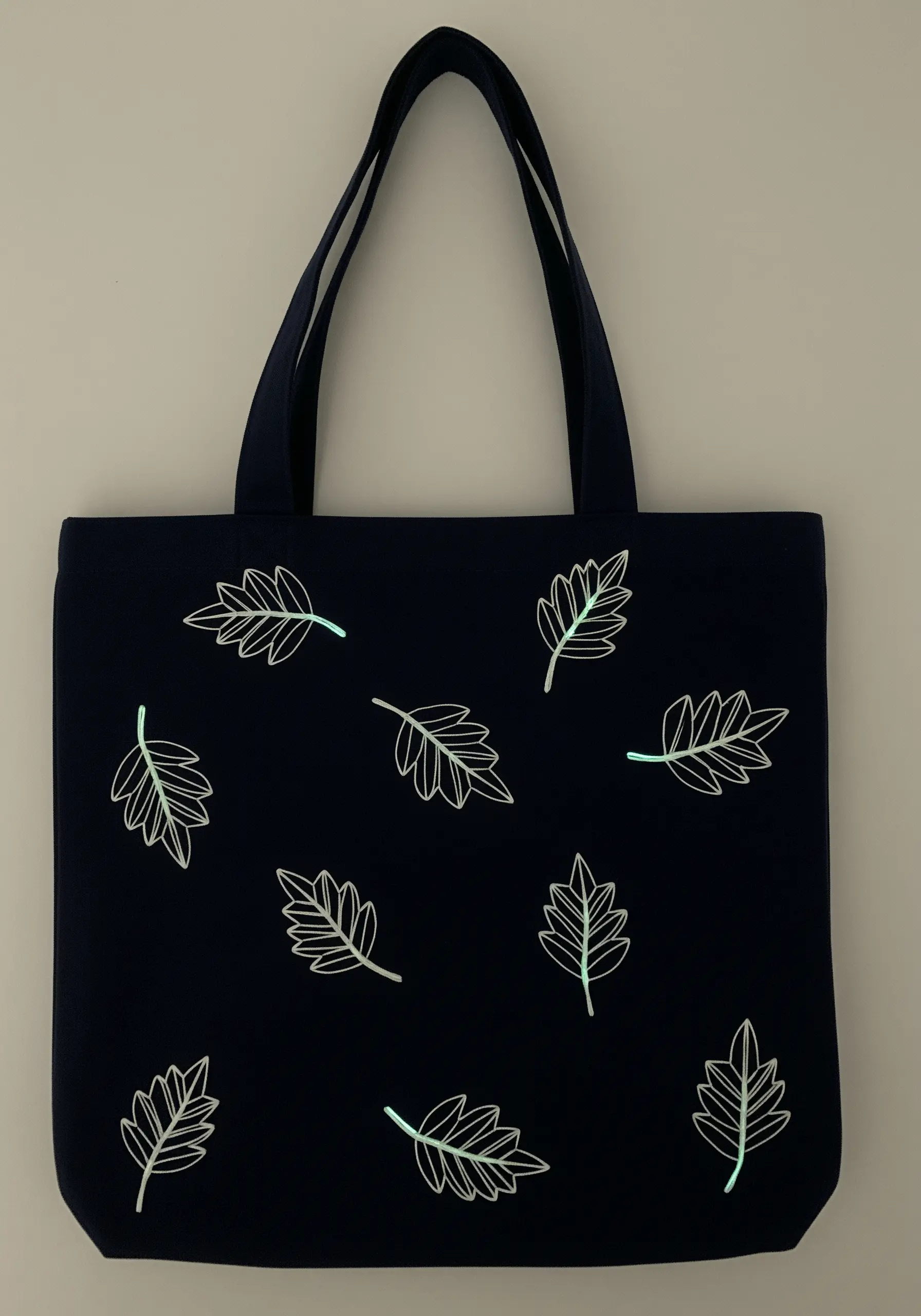 Simple leaf outlines on a dark blue tote bag, stitched with glow-in-the-dark thread.