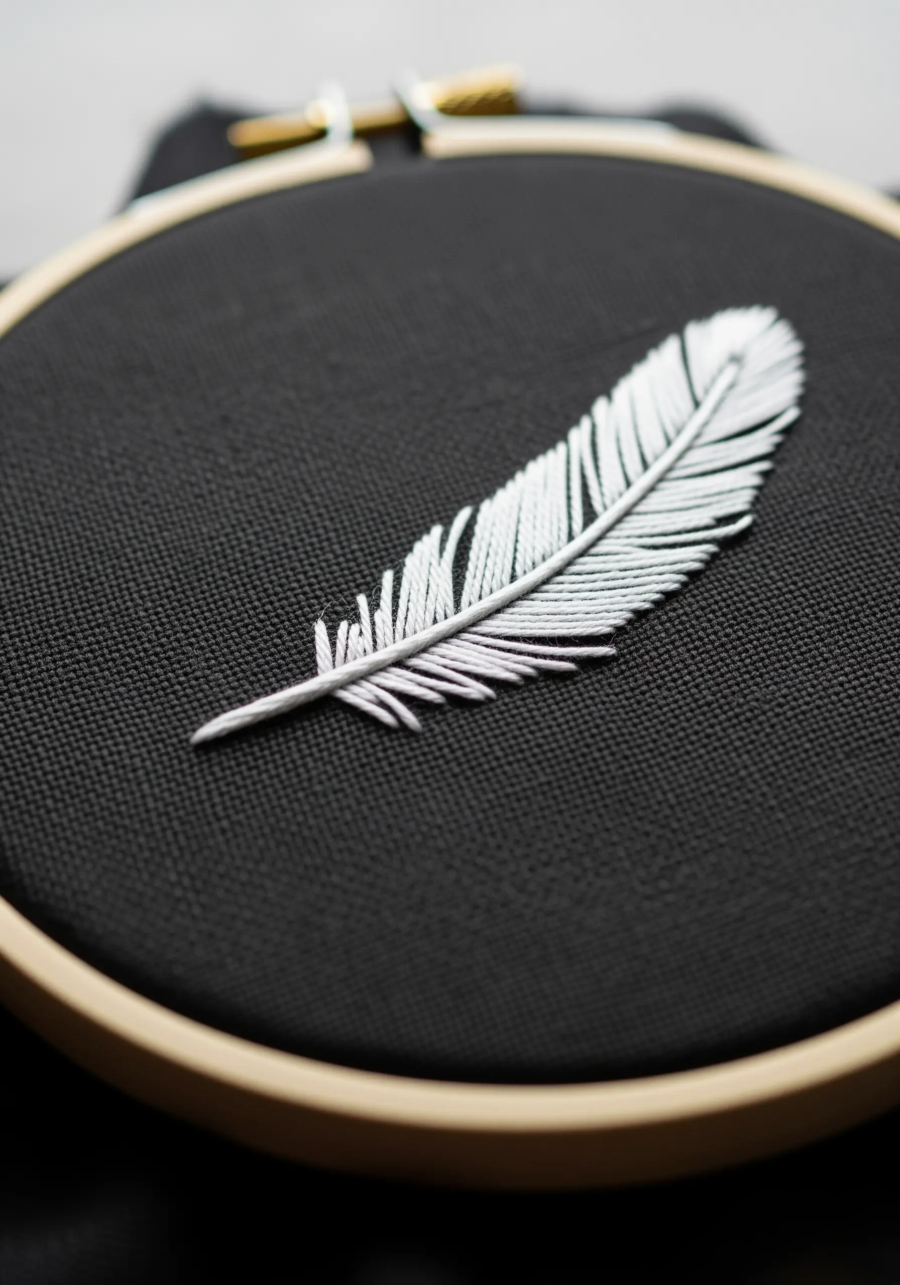 A realistic white feather embroidered on black fabric using angled satin stitches.