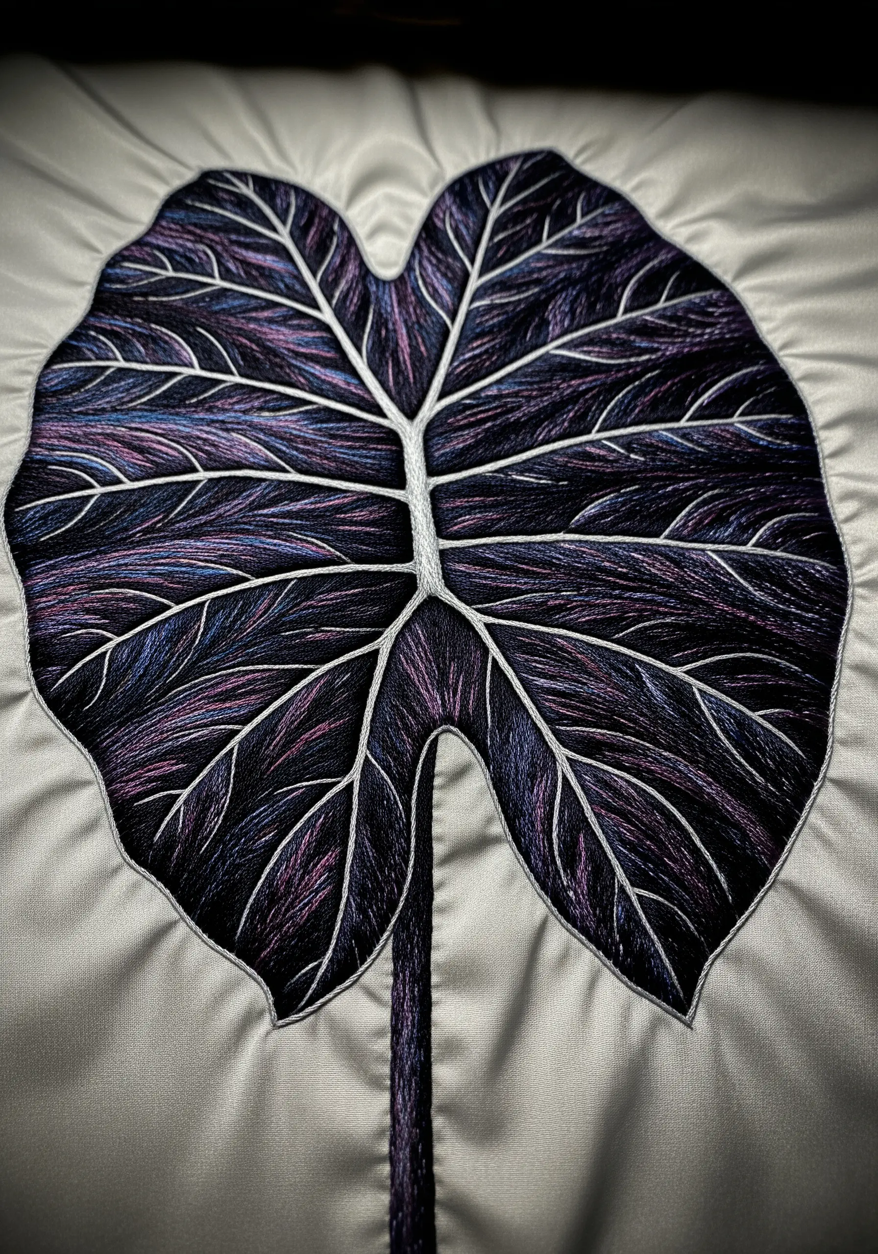 An iridescent Alocasia leaf thread-painted with purple and blue floss on shimmering silver fabric.