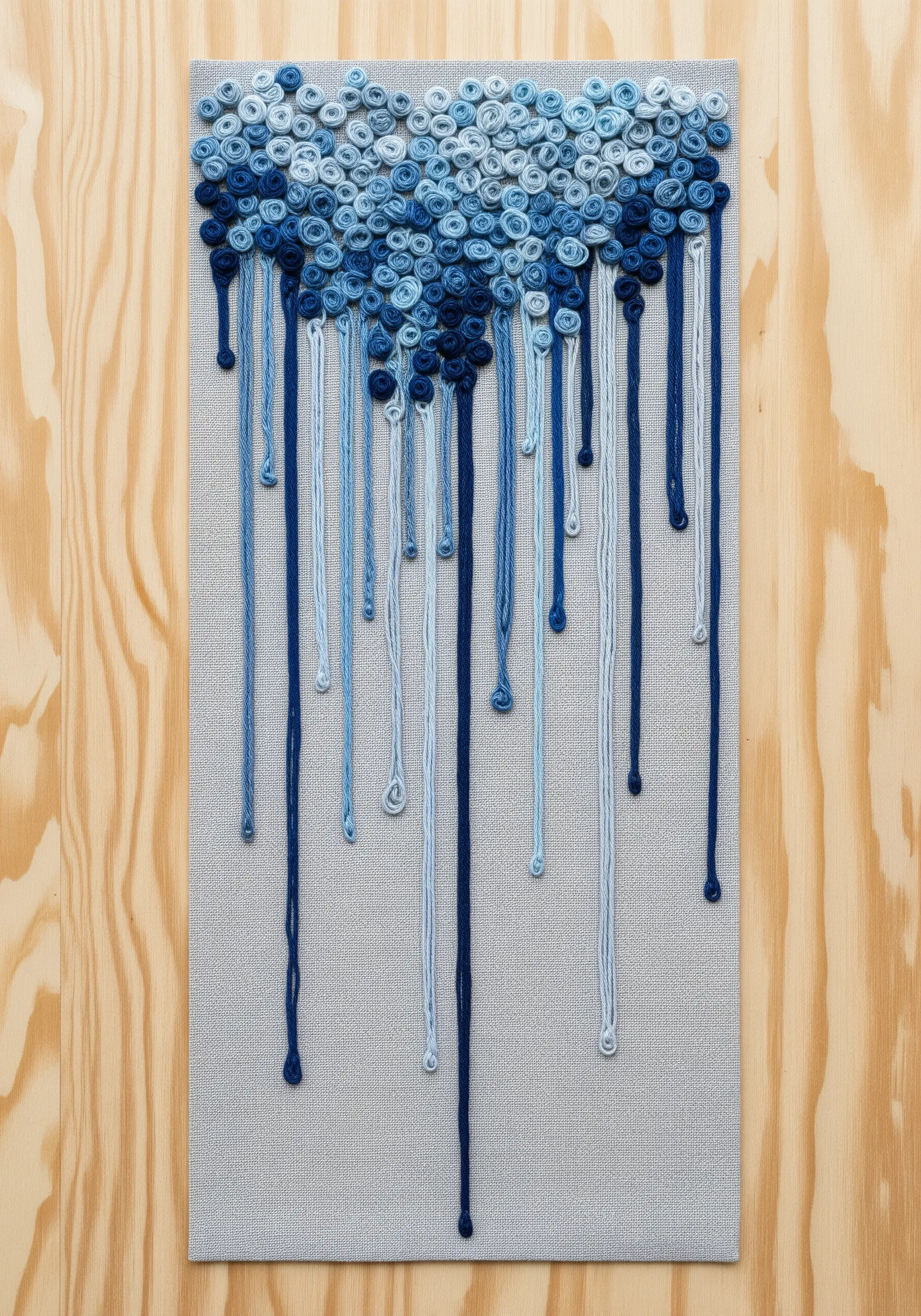 An abstract fiber art piece with blue yarn drips falling from a cloud of coiled knots.