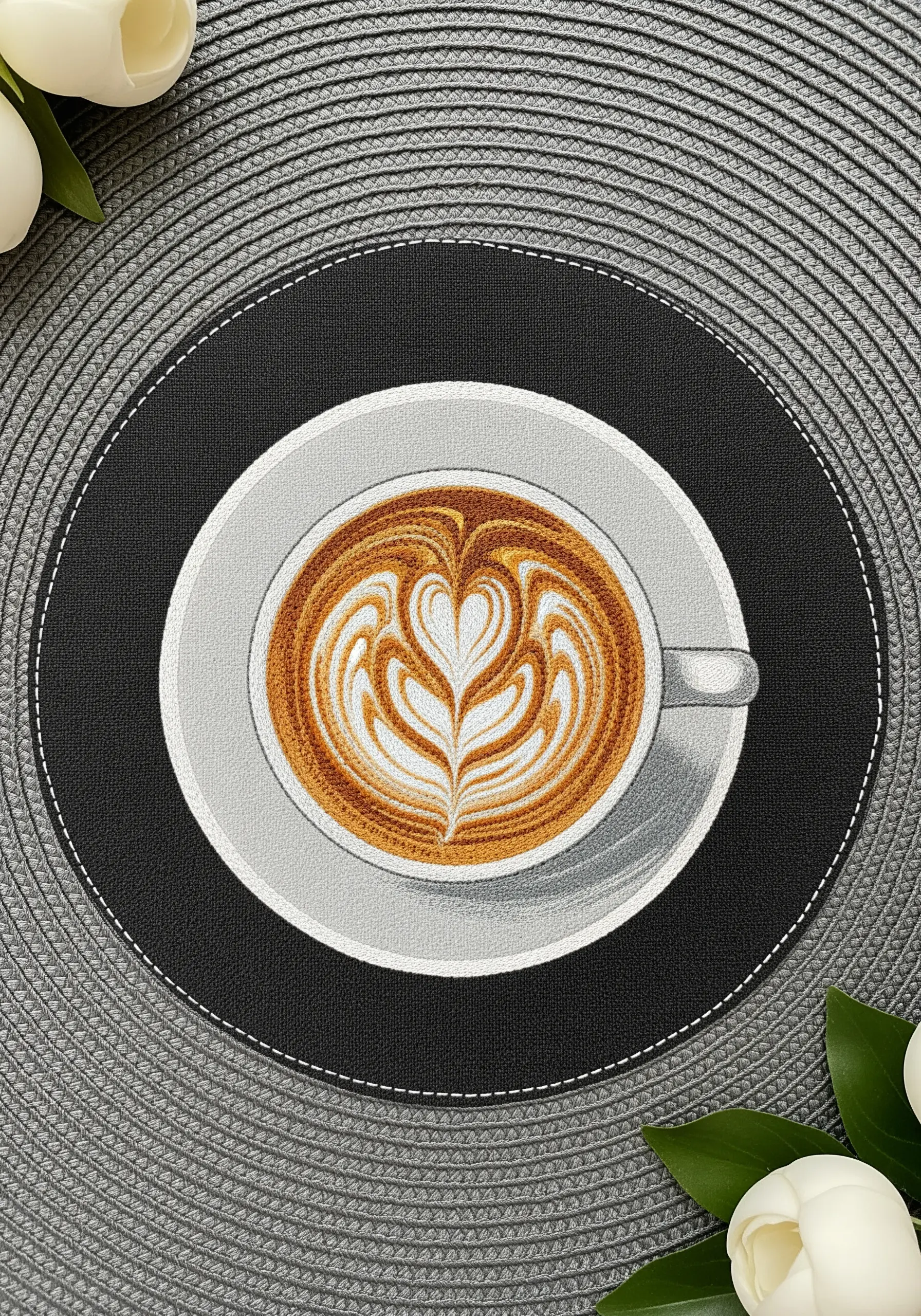Detailed thread-painted latte art in a coffee cup on a circular placemat.