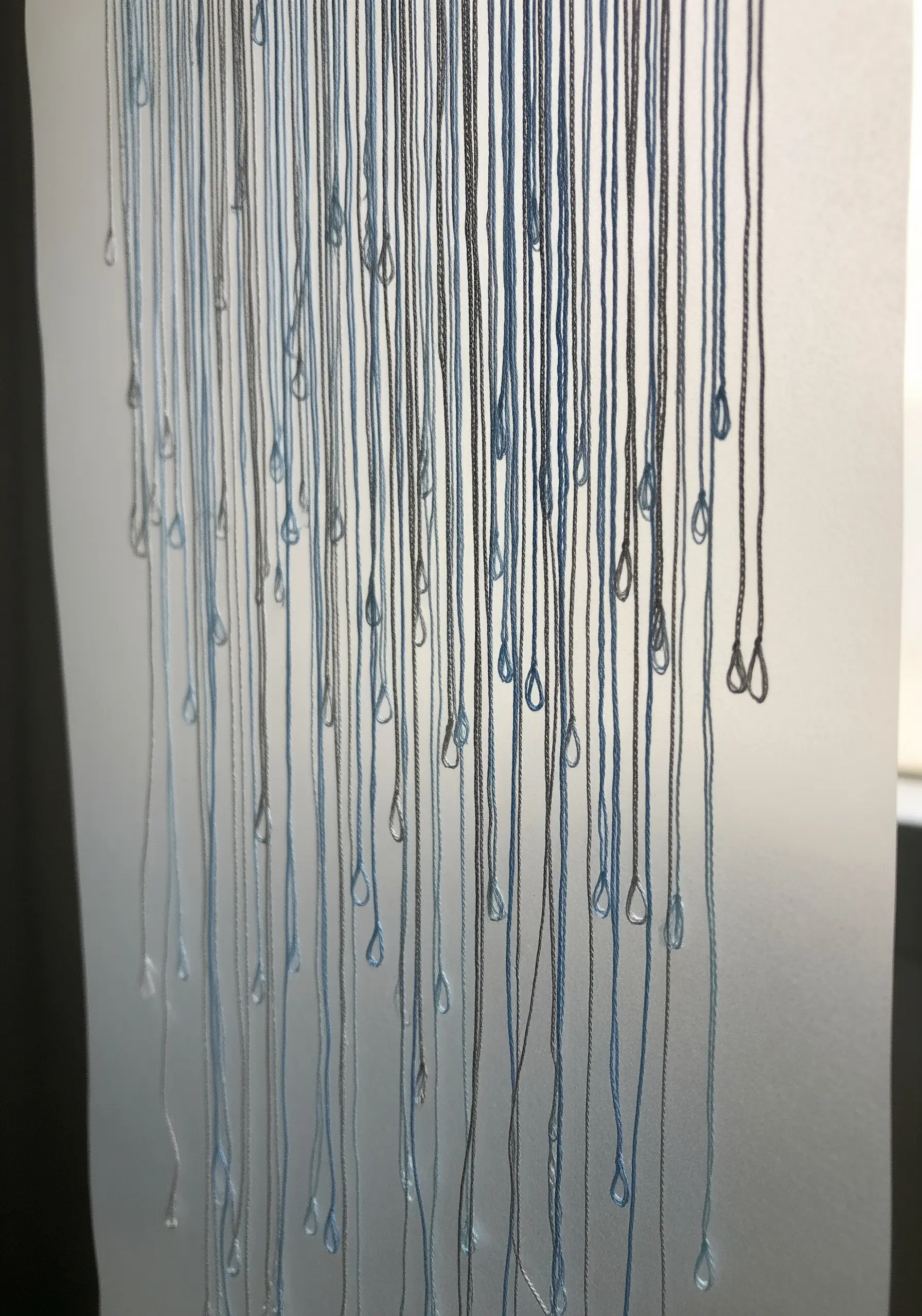 Suspended threads with lazy daisy stitches at the ends to resemble falling raindrops.