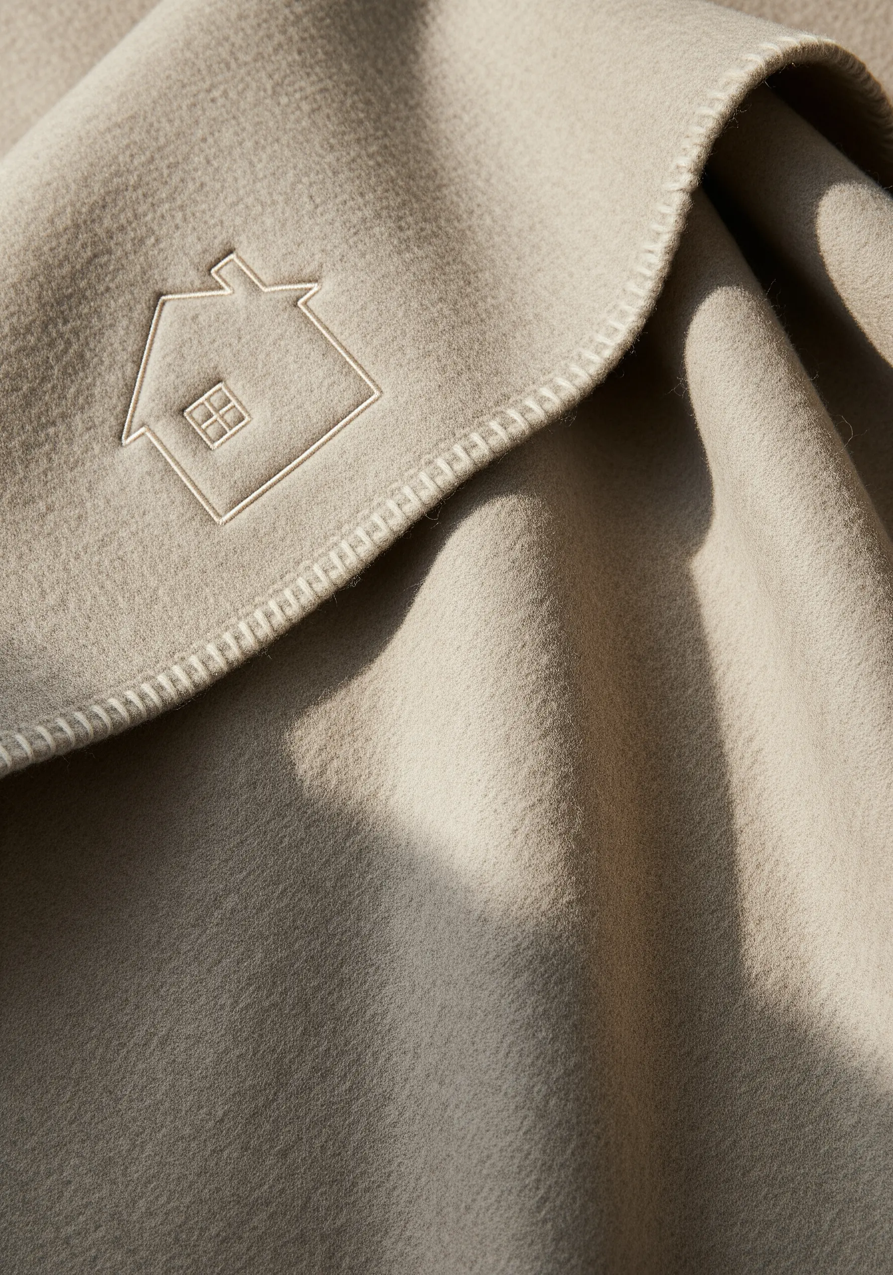 A minimalist house outline embroidered in a light thread on a beige fleece blanket.