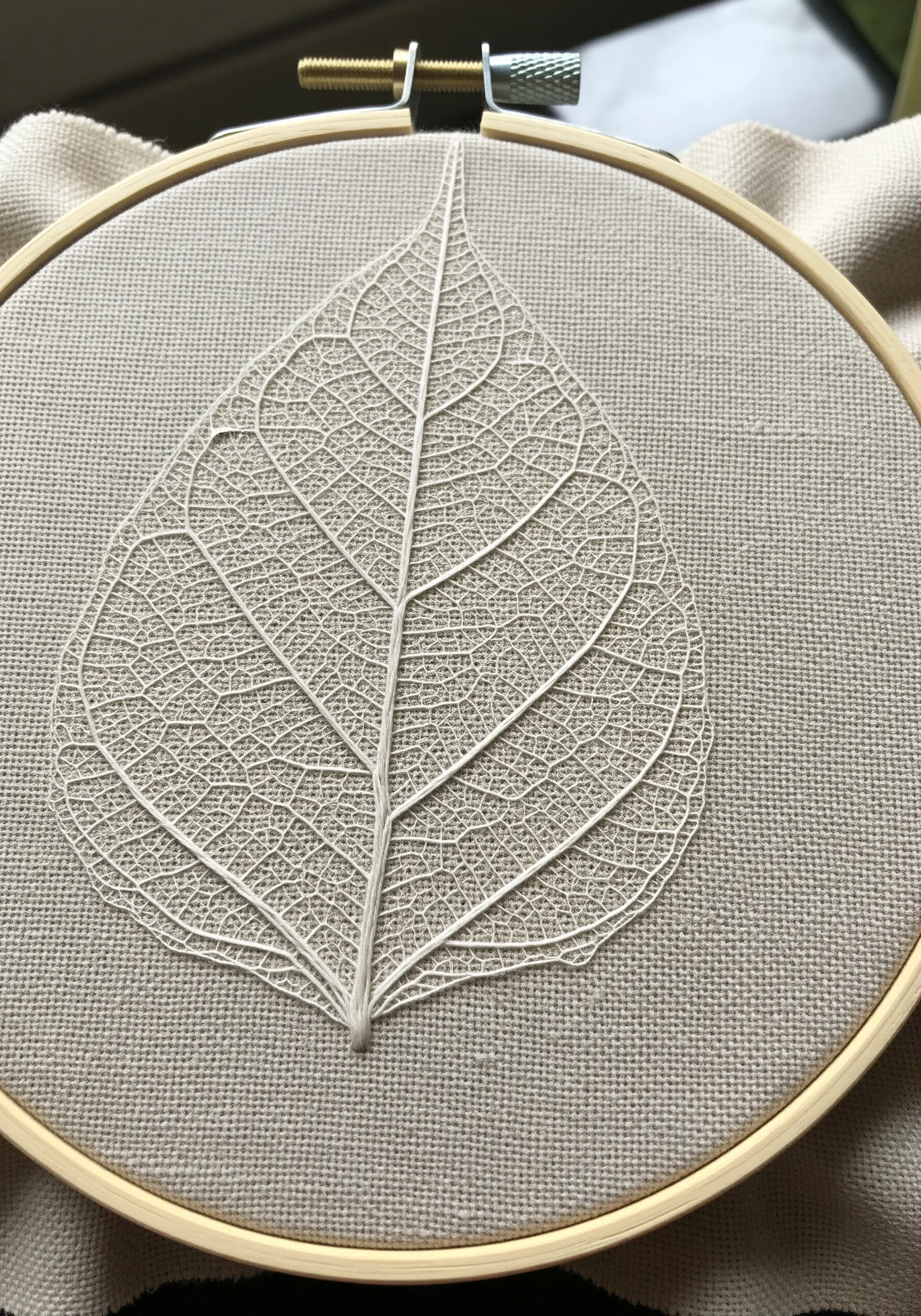 An intricate skeleton leaf embroidered with fine white thread on neutral linen fabric.