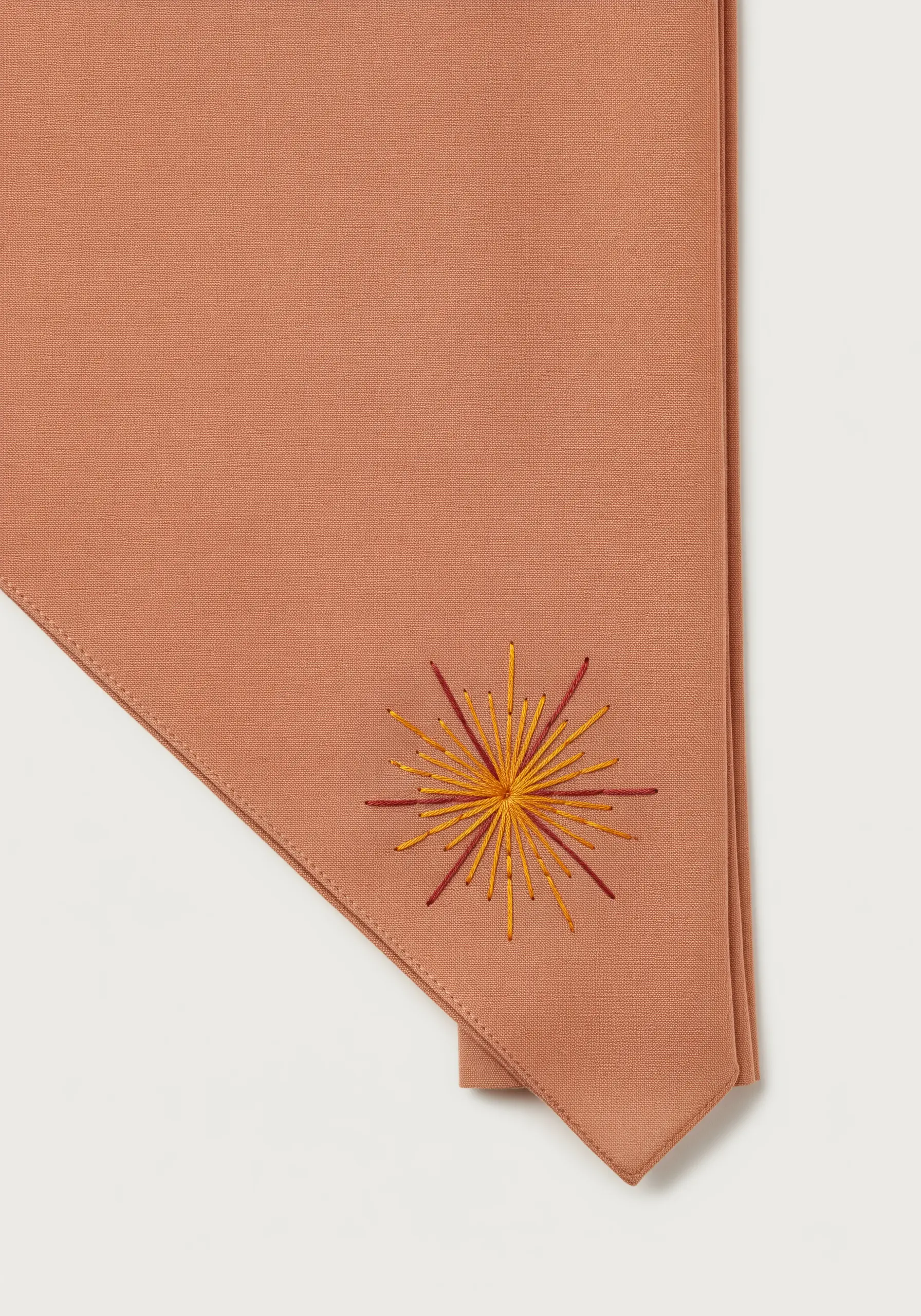 A sunburst motif with radiating straight stitches in yellow and red on a terracotta scarf.