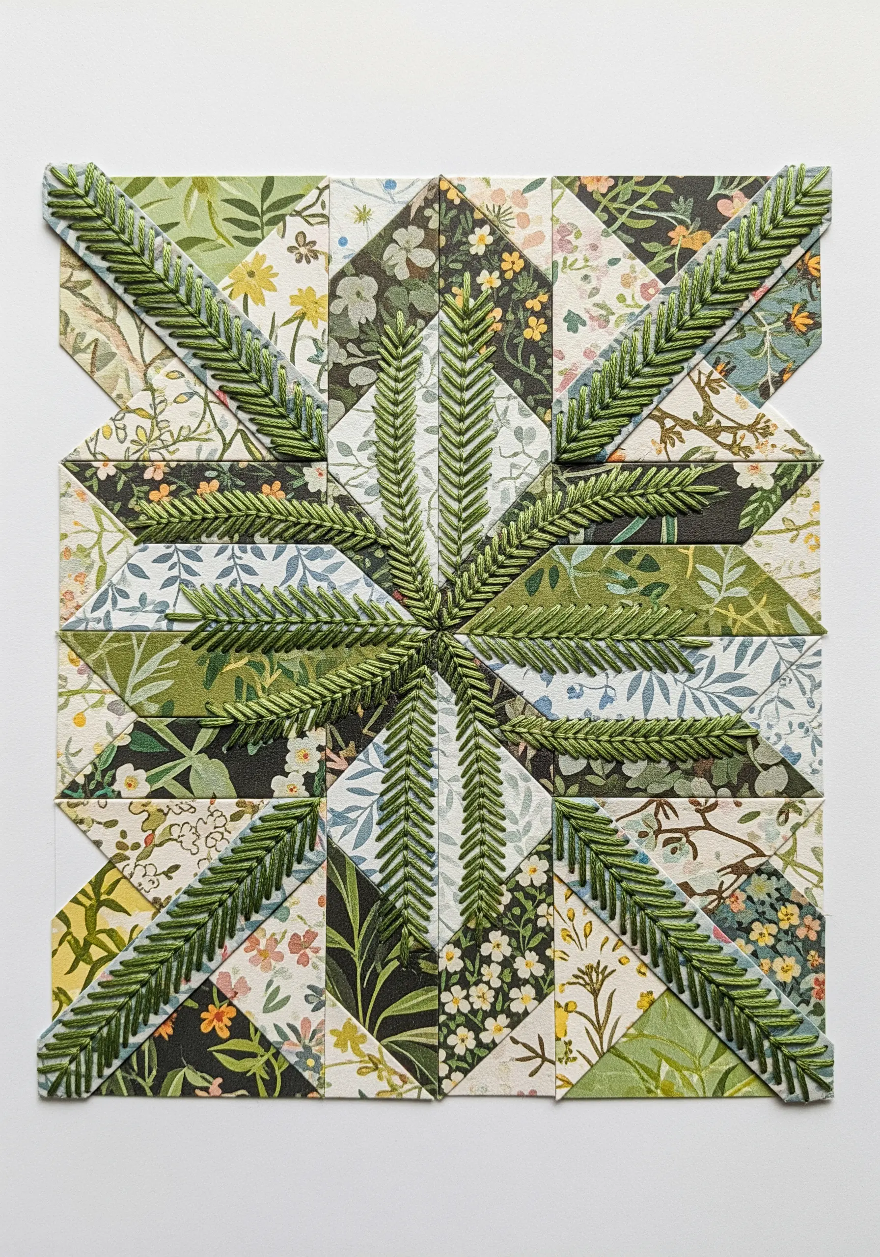 A patchwork of floral and patterned paper squares with a large green fern embroidered over the top.