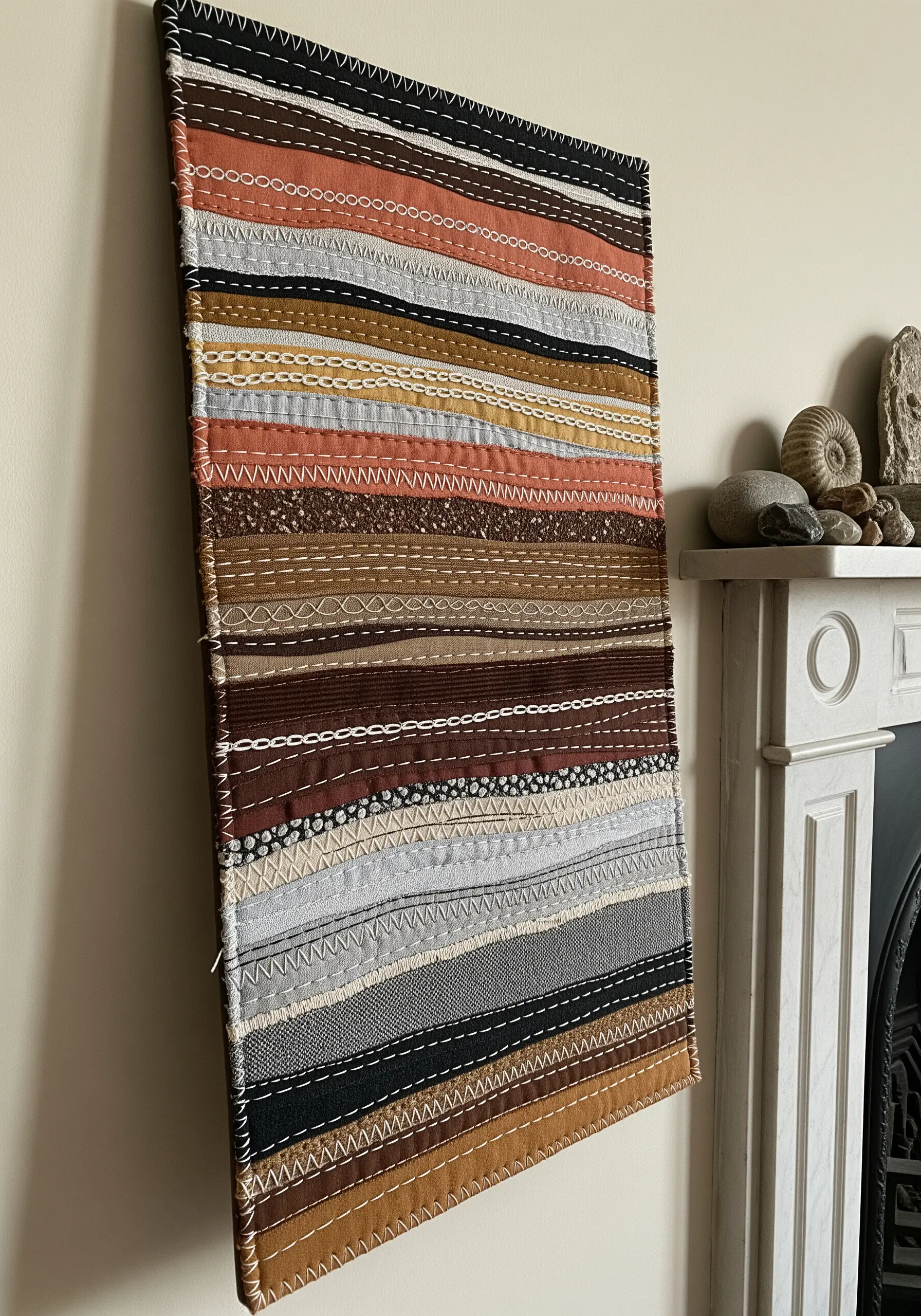 A wall hanging made of colorful fabric strips held together with decorative running stitches.