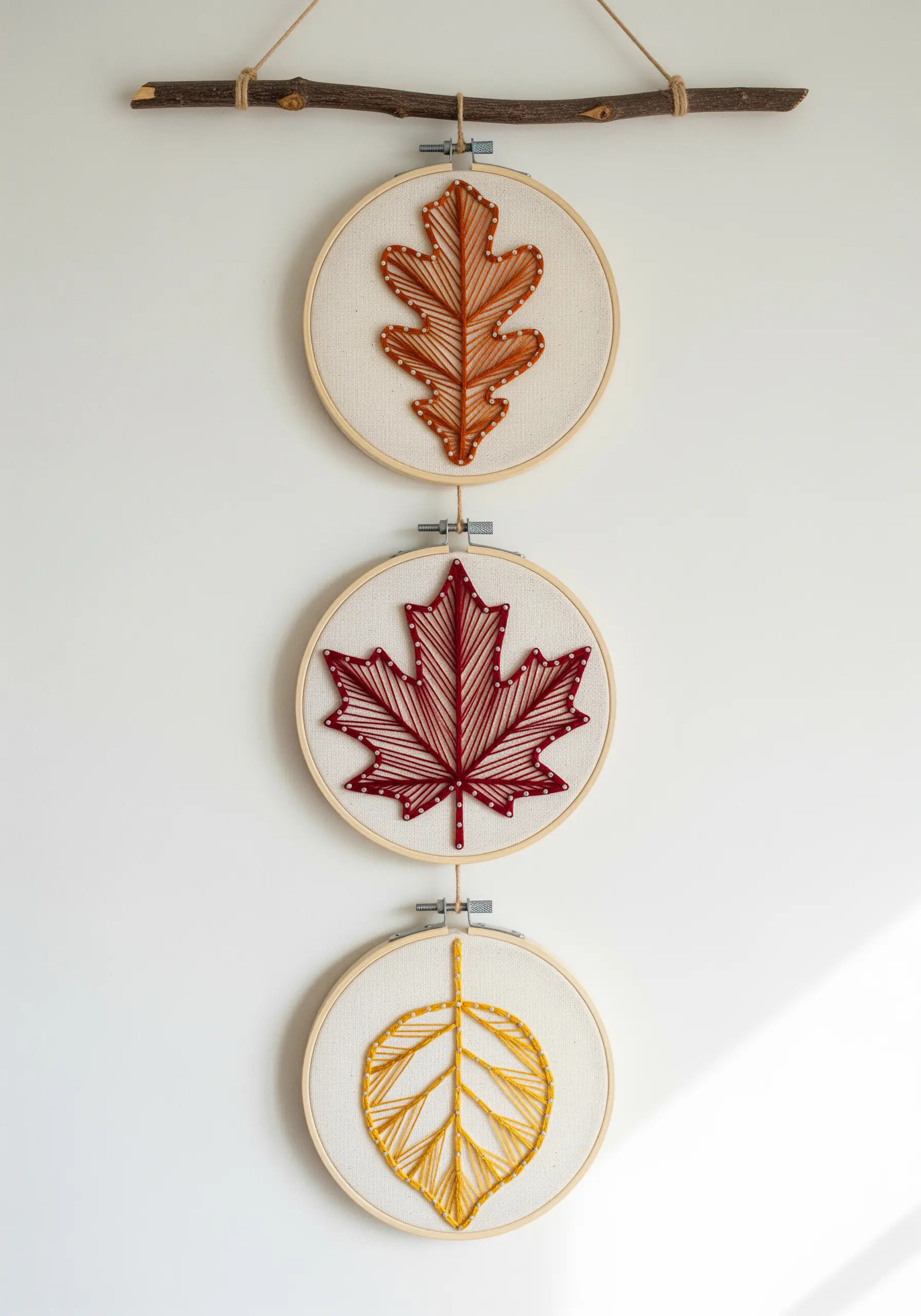Three embroidery hoops displaying string art fall leaves in red, orange, and yellow.