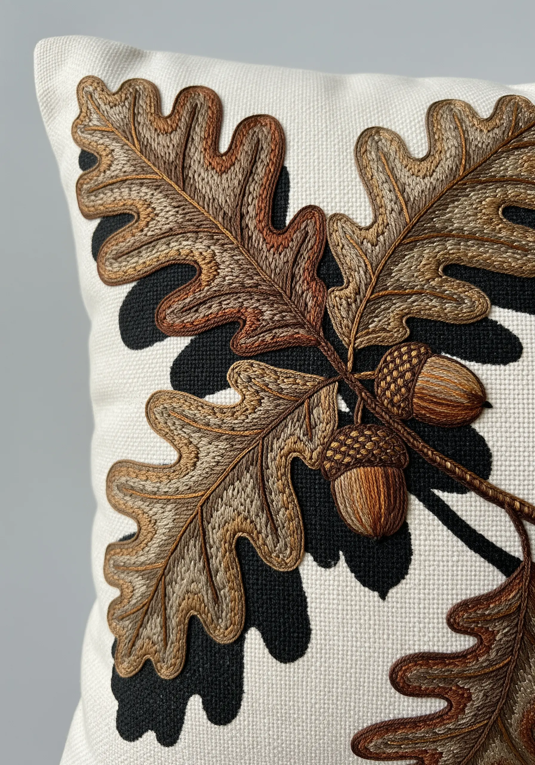 Detailed oak leaf and acorn embroidery on a pillow with a solid black shadow.