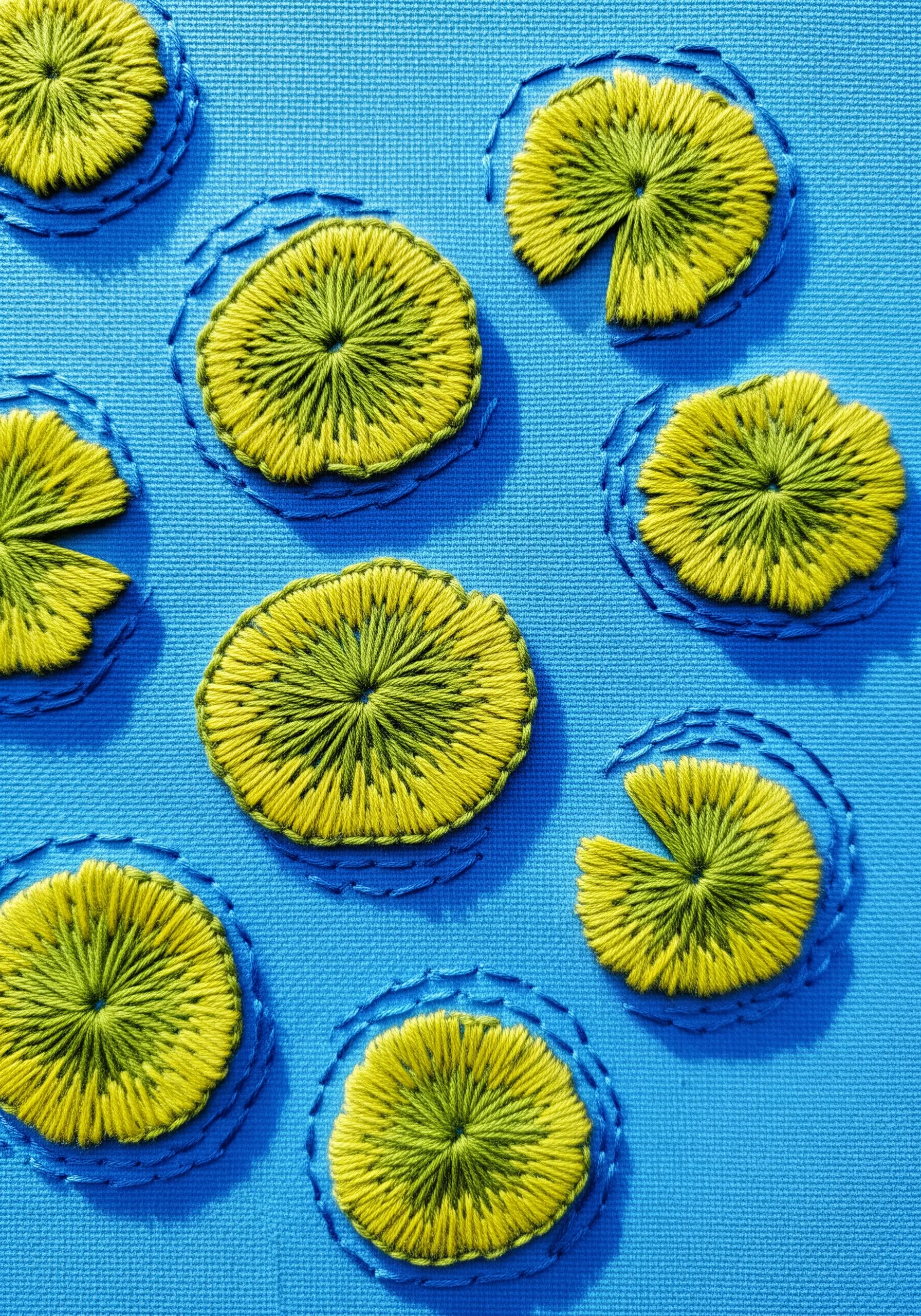 Embroidered lily pads on a blue background, with stitched blue circles indicating water ripples.