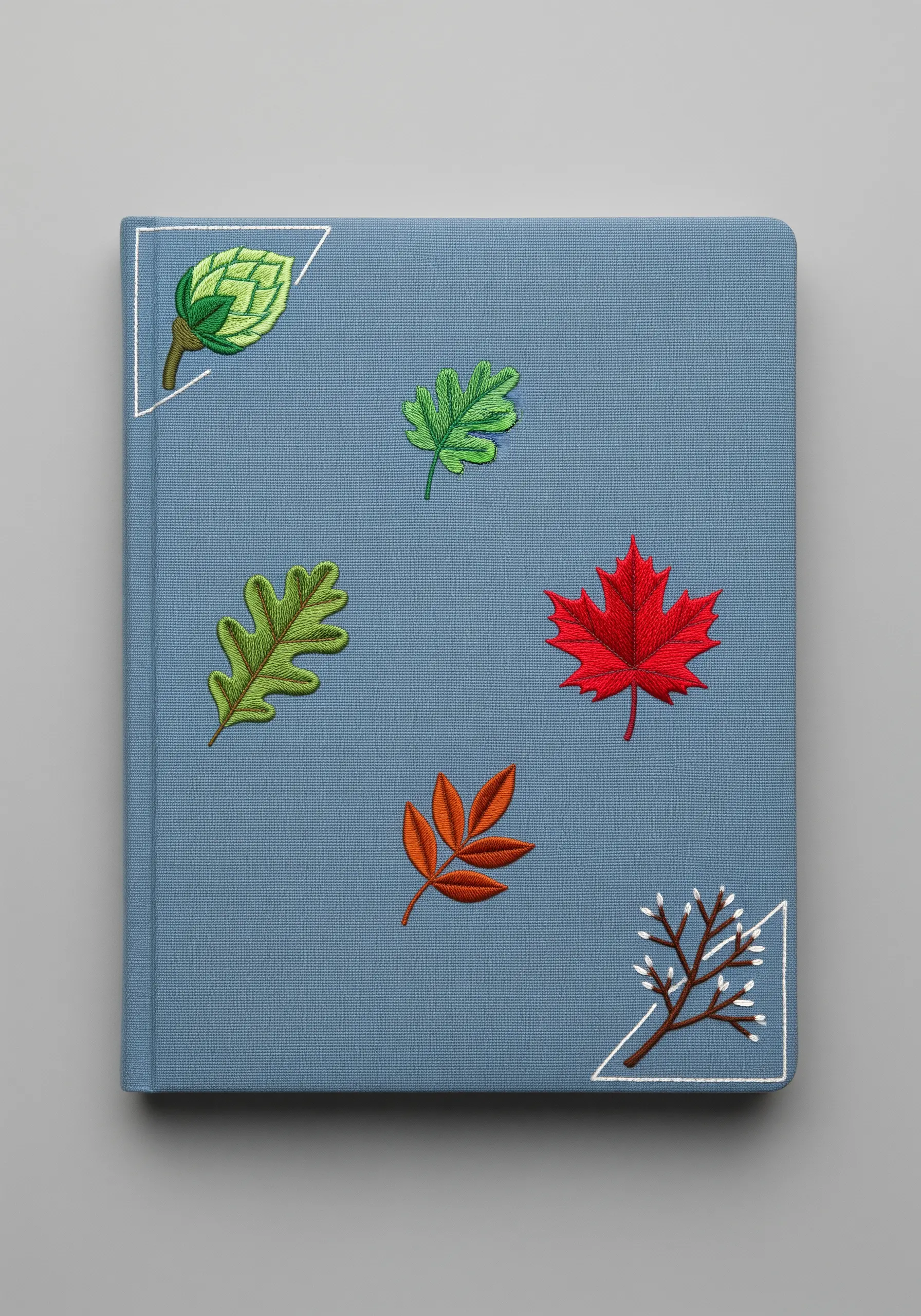 Several different types of embroidered leaves appliquéd onto a blue journal cover.