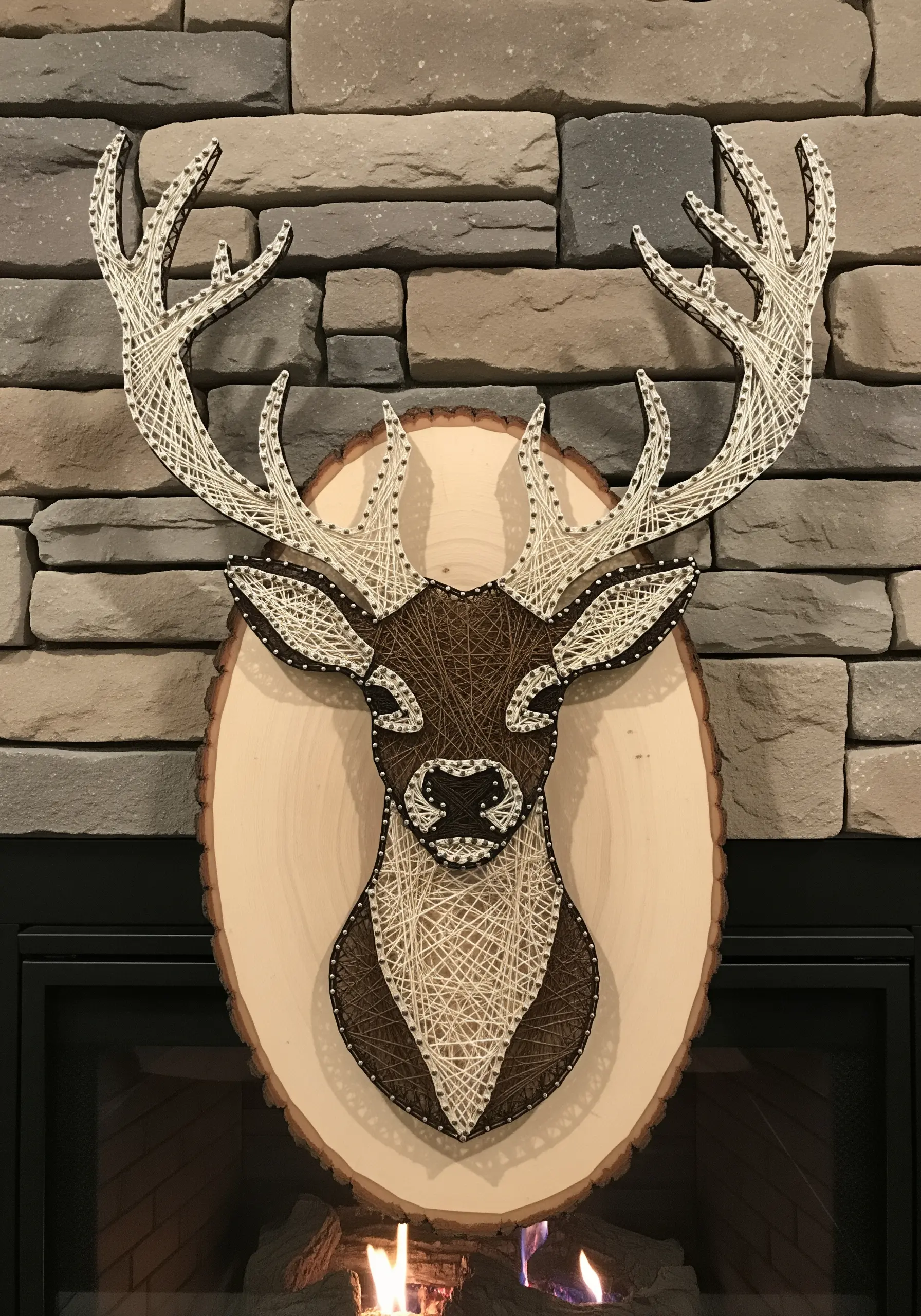 String art of a deer's head in brown and white on a wood slice against a stone wall