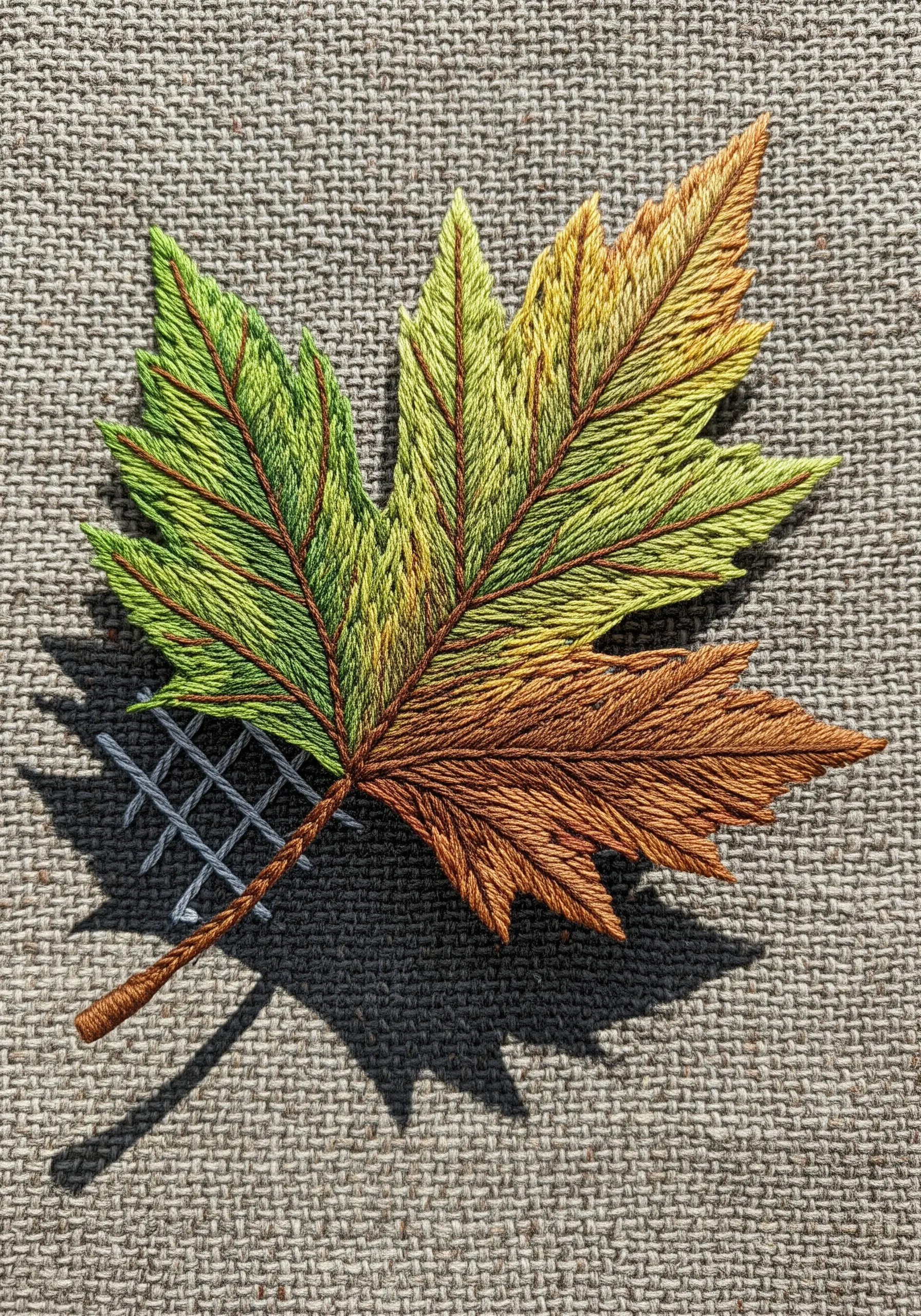 A maple leaf embroidered on burlap with a shadow created from gray cross-hatched stitches.