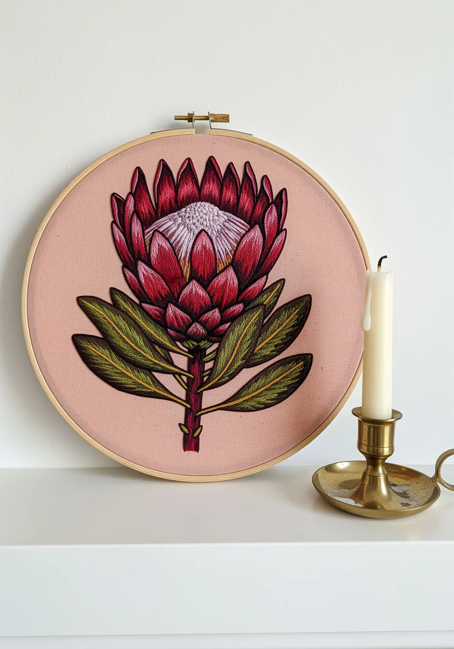 Realistic protea flower embroidery with detailed thread painting on pink fabric.