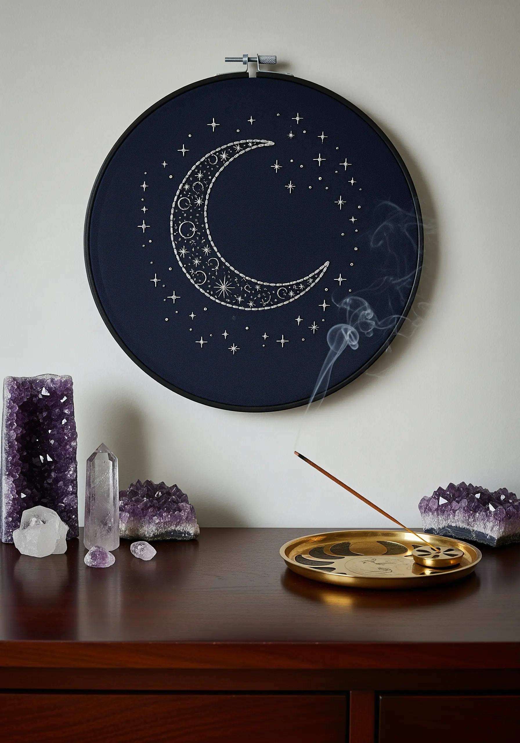 A crescent moon and stars embroidered in white thread on dark navy fabric in a black hoop.