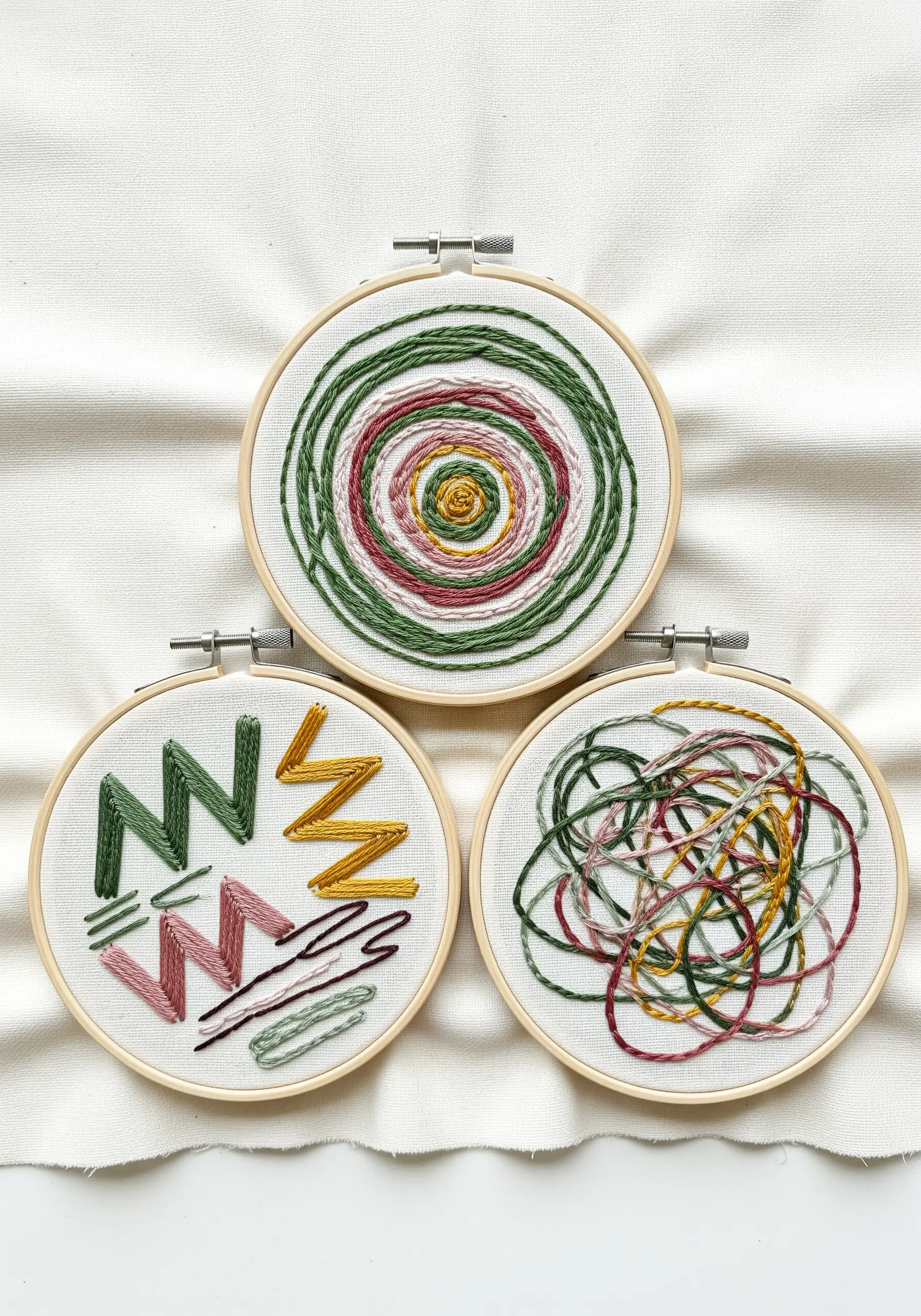 Three embroidery hoops displaying different abstract stitch studies: spirals, zigzags, and scribbles.