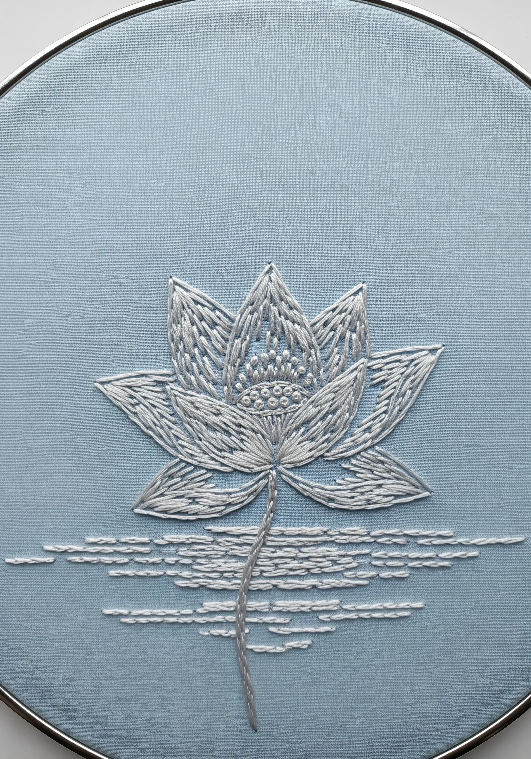 A white lotus flower embroidered on light blue fabric using spaced-out satin stitches.