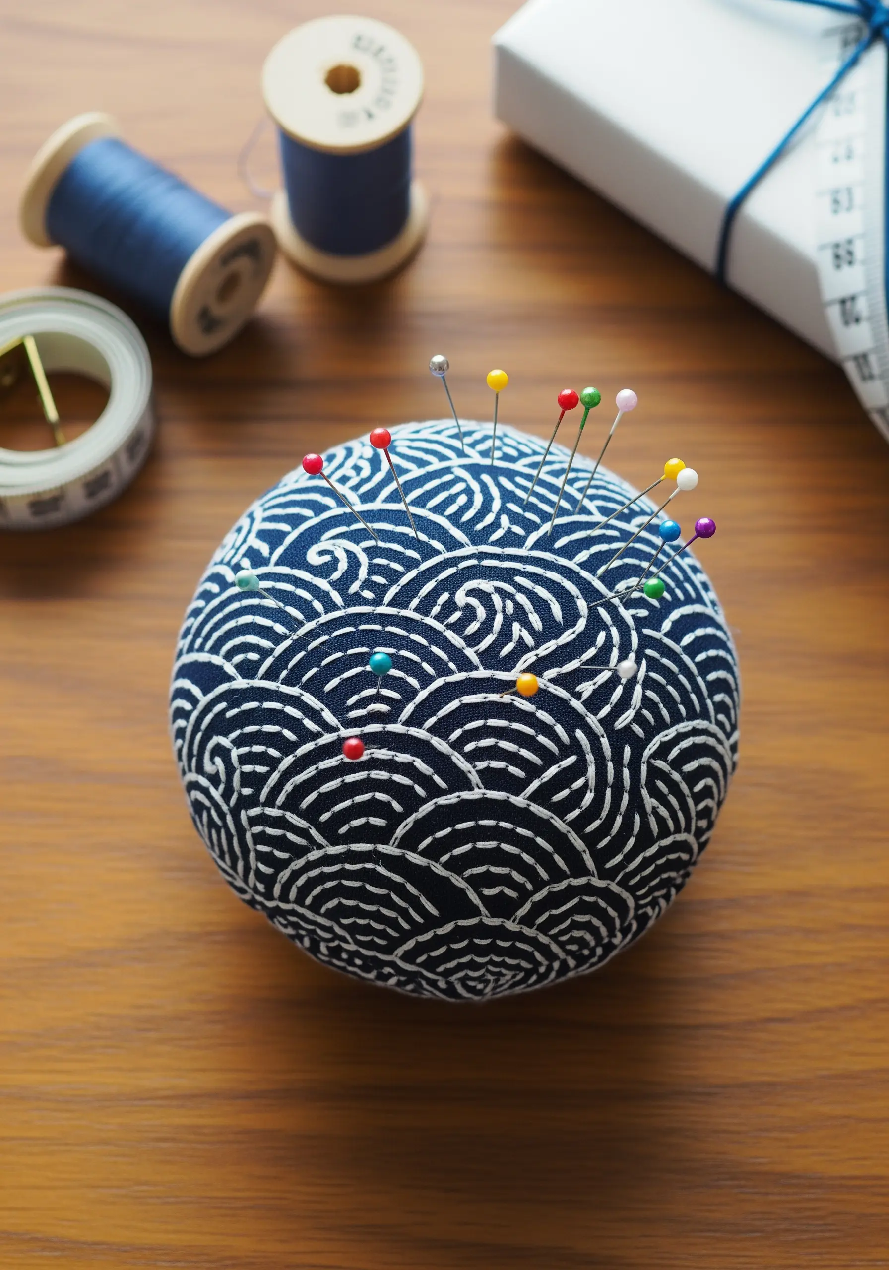 A round pincushion covered in a Japanese wave print fabric, with colorful pins stuck in it.
