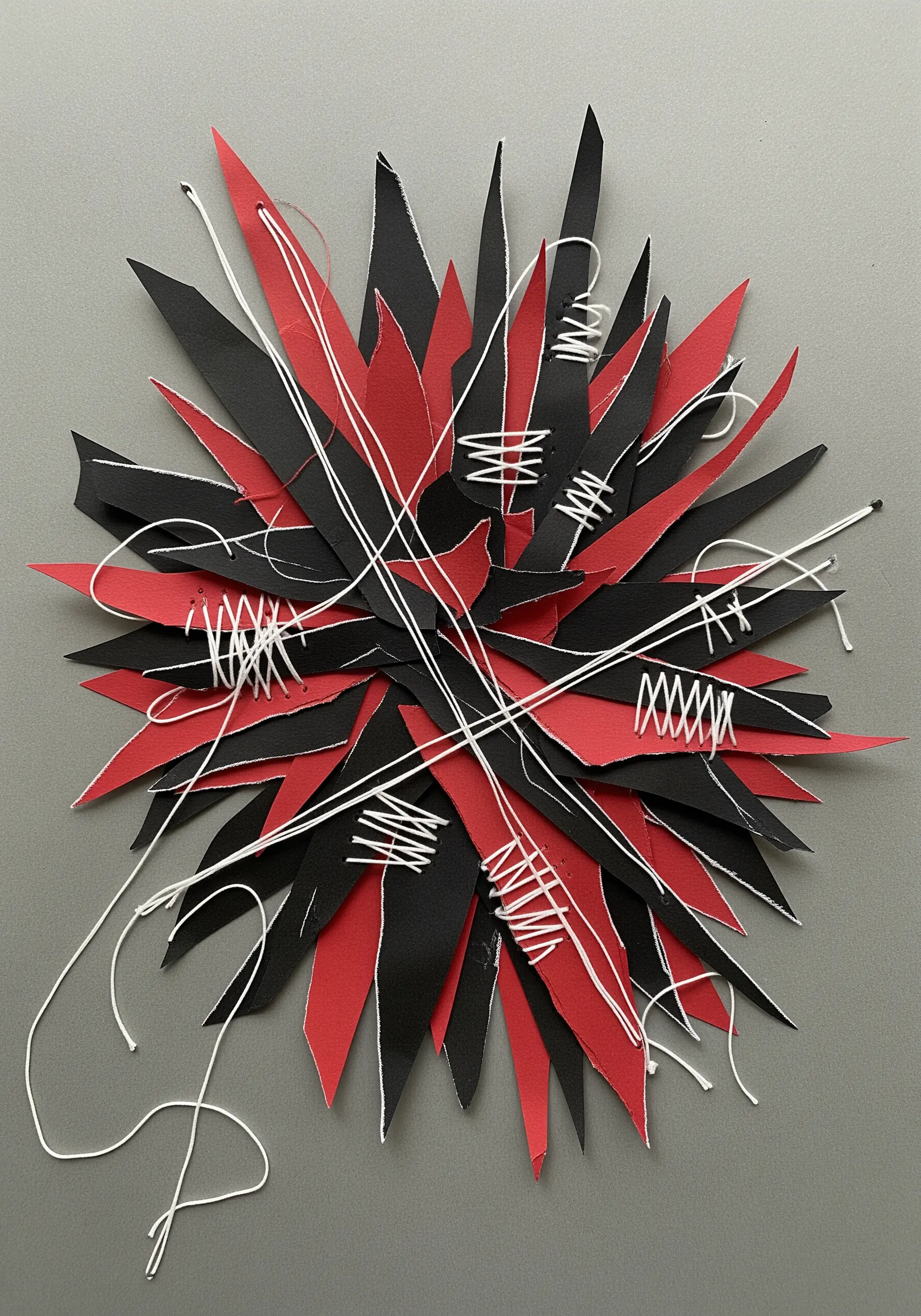 An abstract burst of red and black paper shards with chaotic, expressive white stitches.
