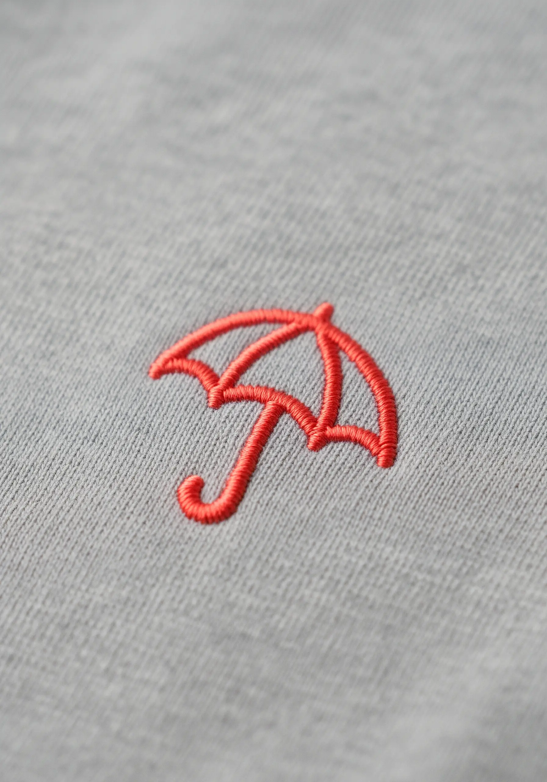 A coral-colored umbrella embroidered on a gray shirt, with varied stitch widths for the outline.