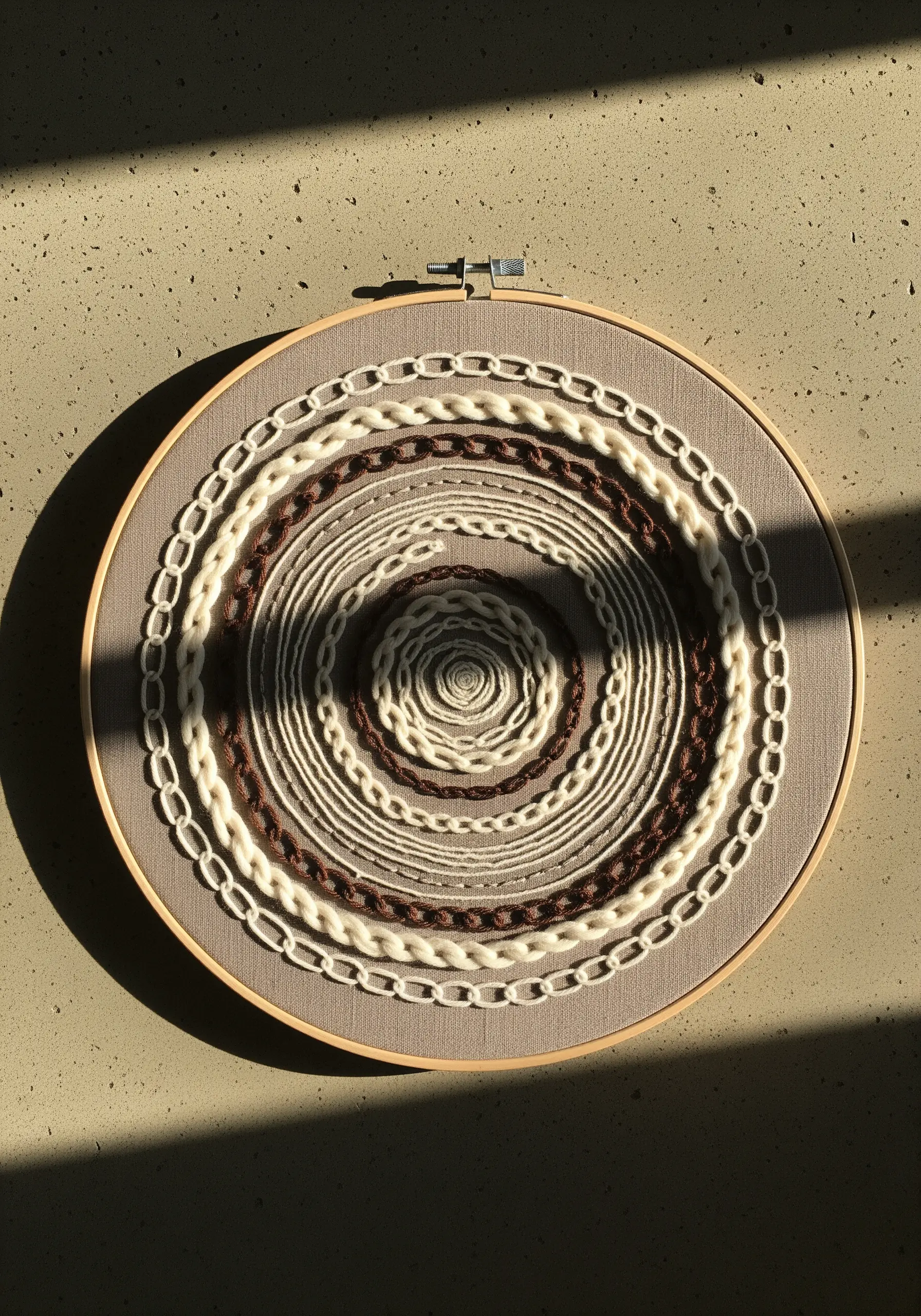 A circular embroidery with concentric rings of textured stitches in brown, white, and cream.