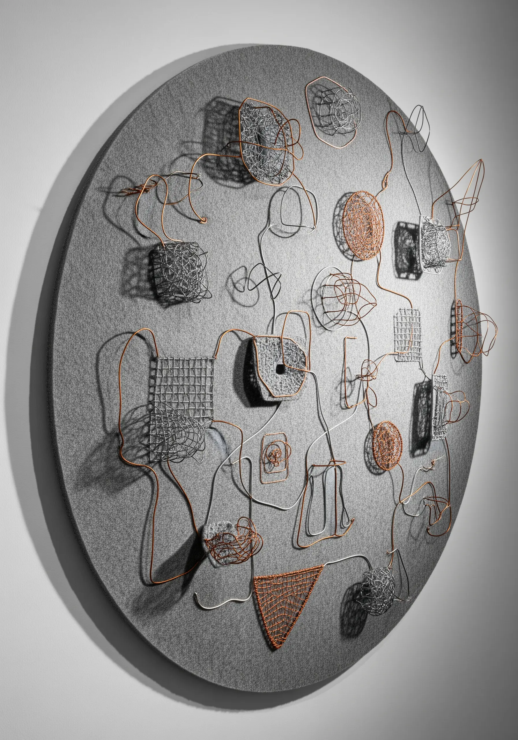 A round wall sculpture made from bent wire, with sections filled in with woven and wrapped thread.