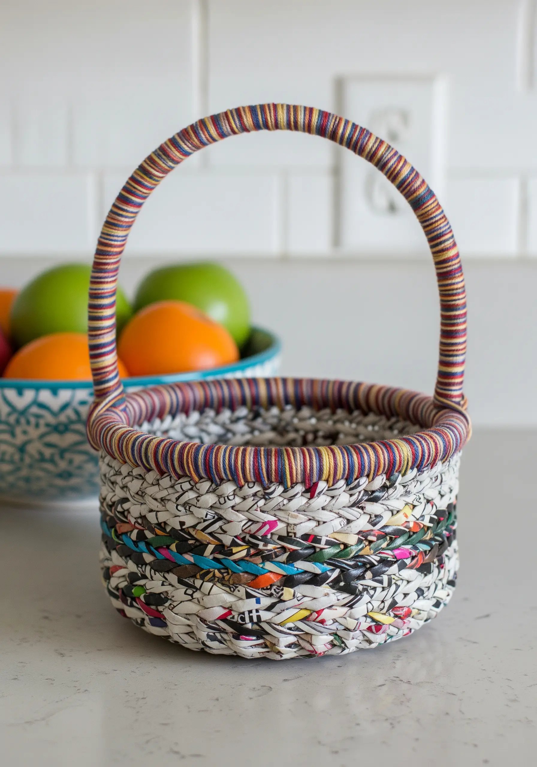 A small woven basket made from recycled newspaper strips that have been wrapped in colorful thread.