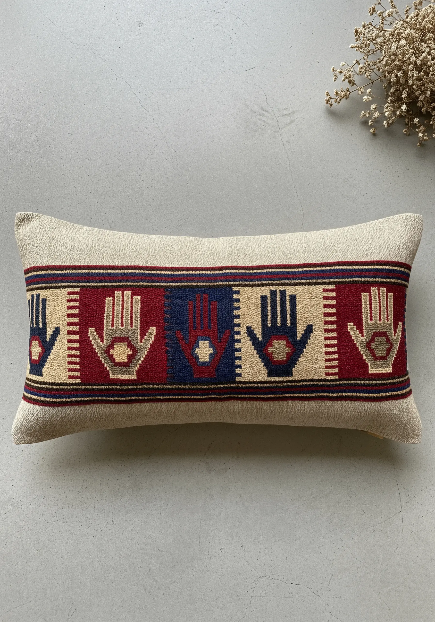A lumbar cushion with a band of Hamsa hands stitched in a woven, color-blocked style