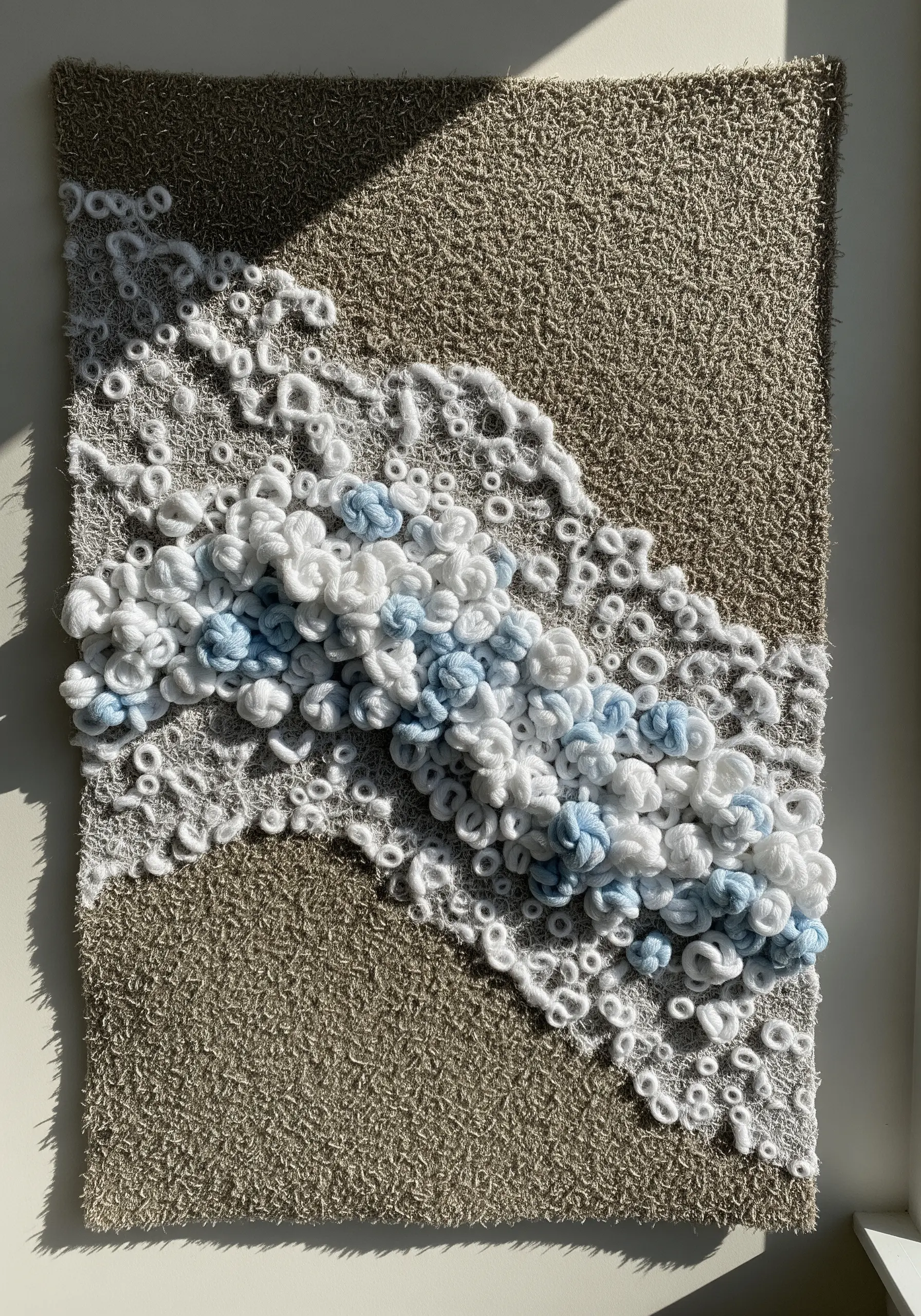 A textural wall hanging of sea foam made with chunky white and blue yarn loops.