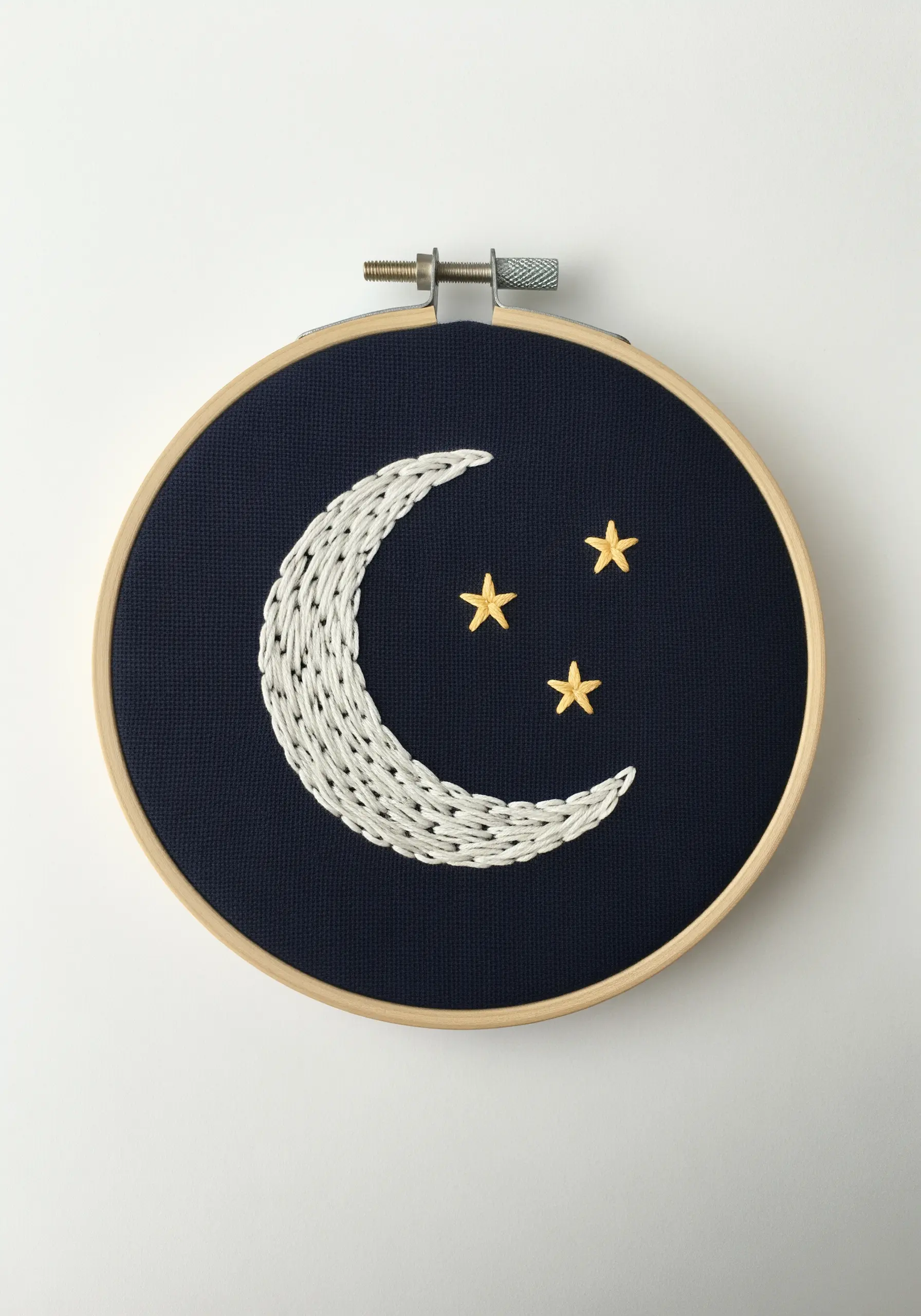 A textured crescent moon with woven-style stitches and three yellow stars on navy fabric.