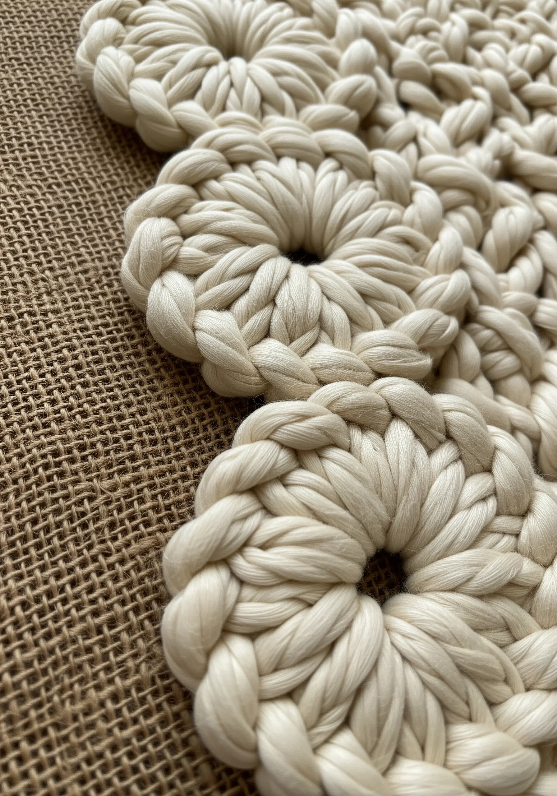 Thick, cream-colored yarn woven into floral medallions on a burlap background.