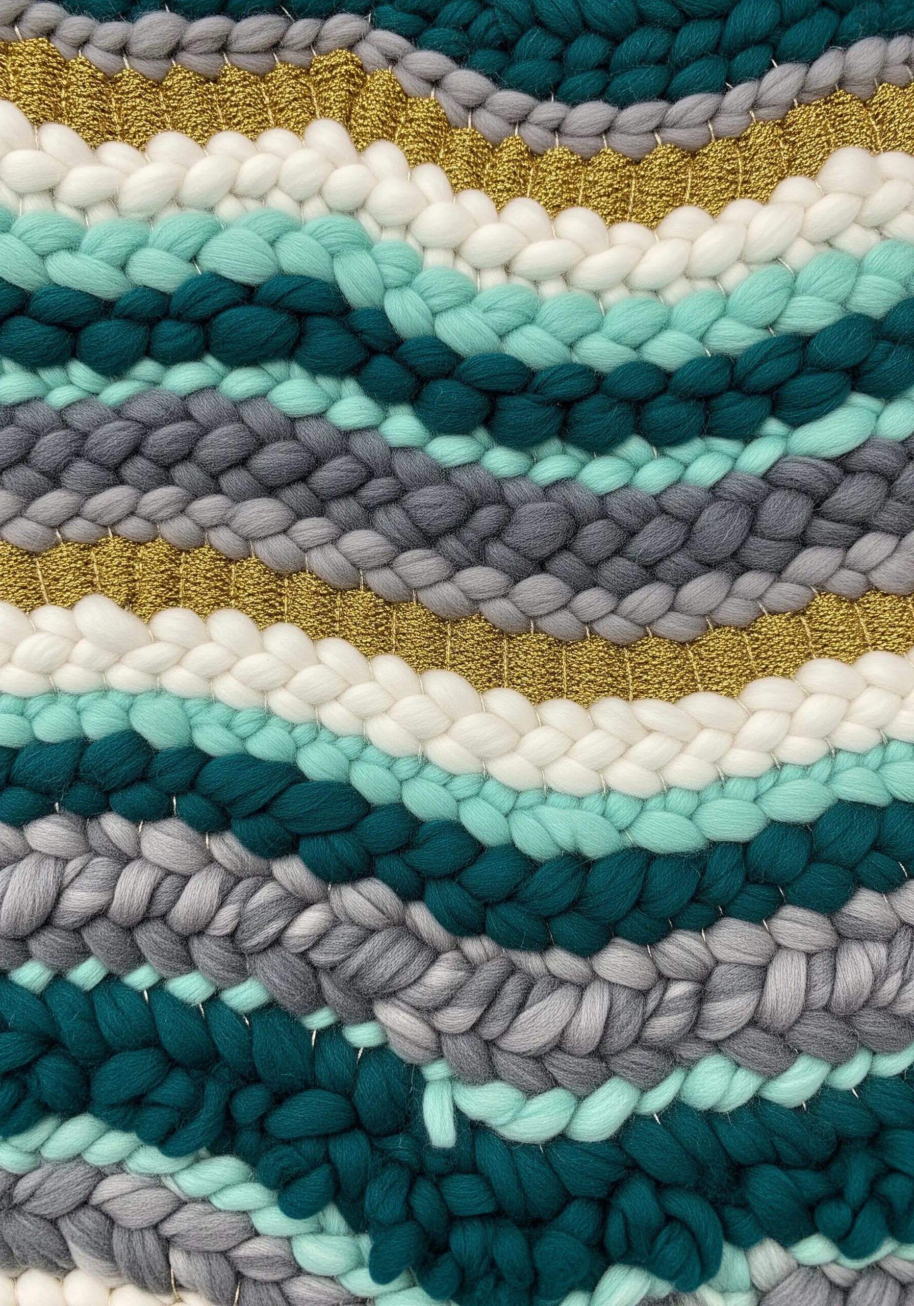 A close-up of a woven piece with thick wool braids and thin metallic gold thread.