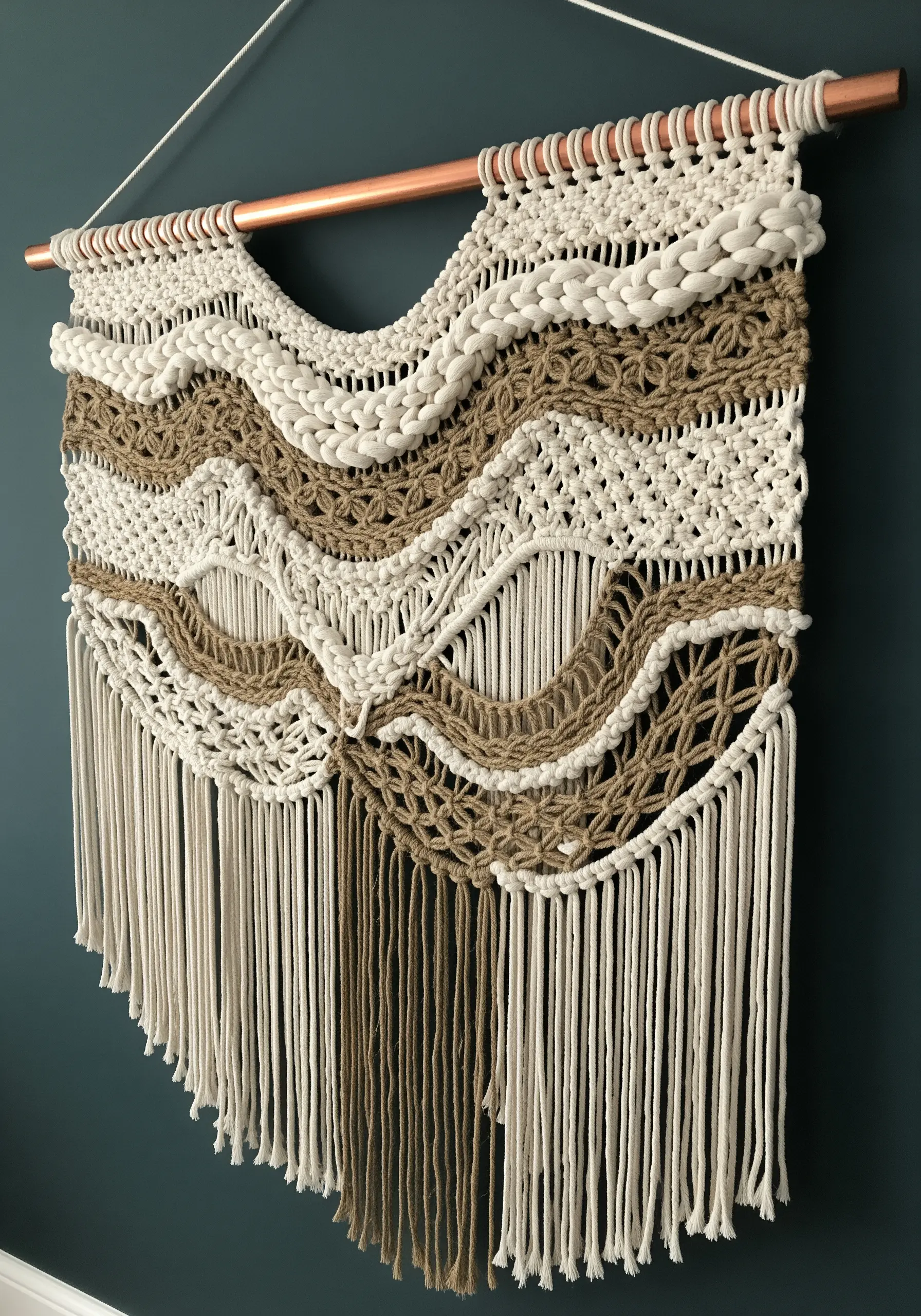 Macrame wall hanging with layered knots and natural jute on a copper rod.