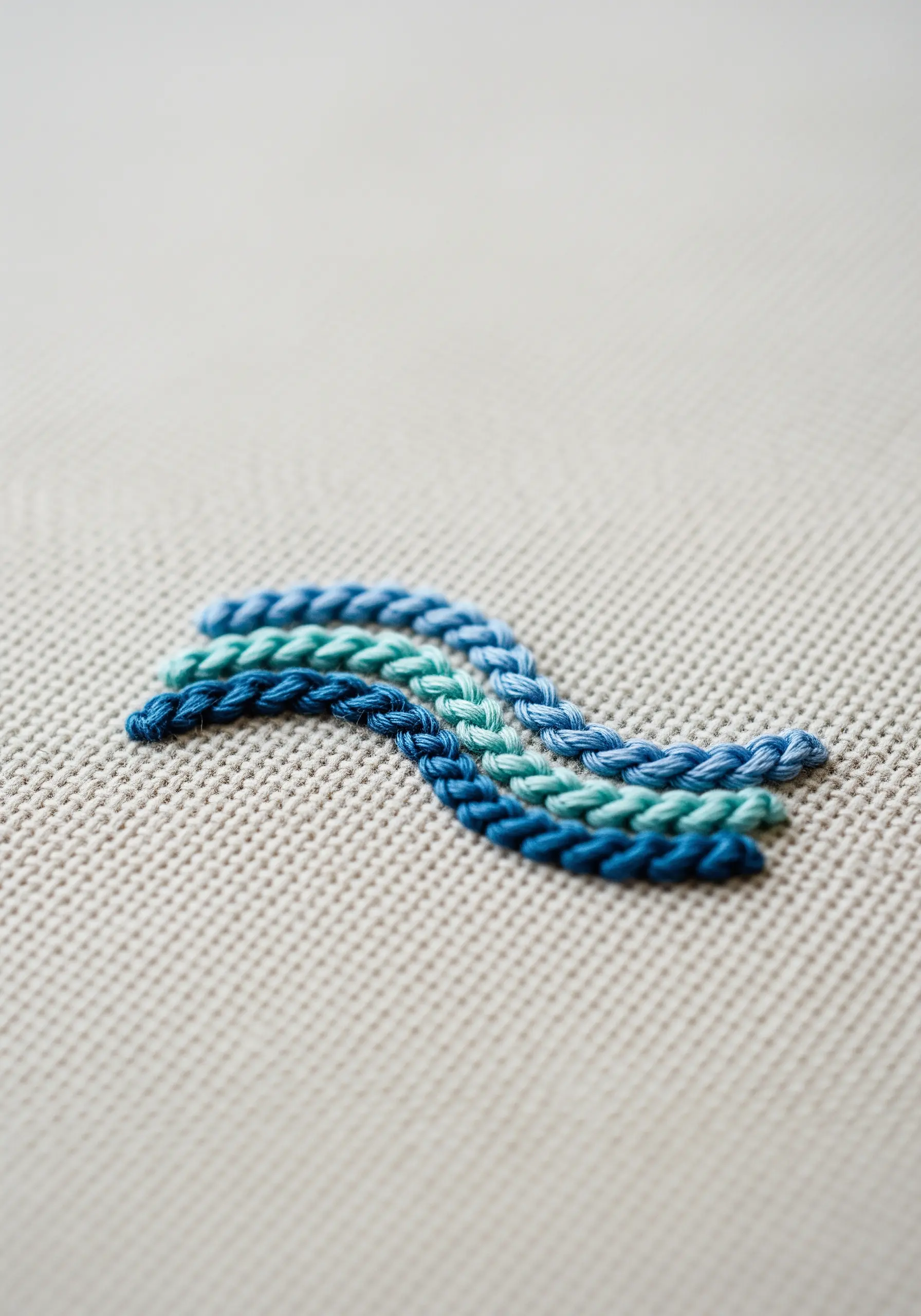 A close-up of a woven, braid-like embroidery stitch using multiple shades of blue thread.