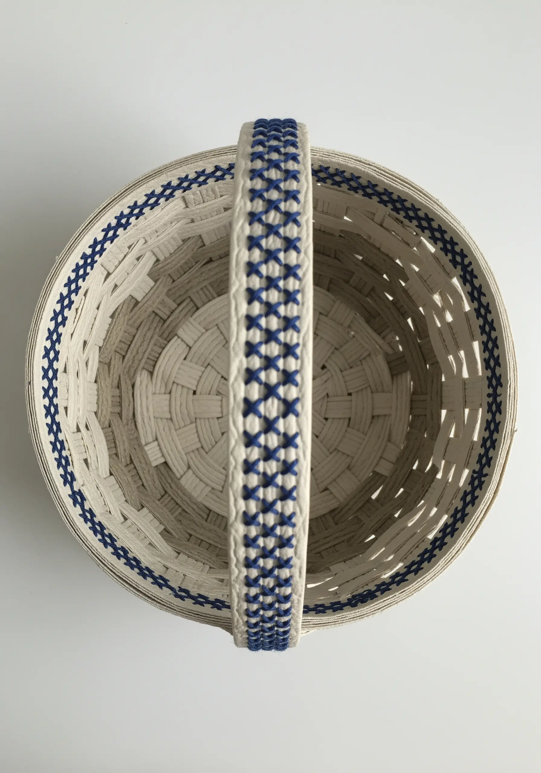 A woven paper basket with a blue and white cross-stitch pattern on the handle and rim.