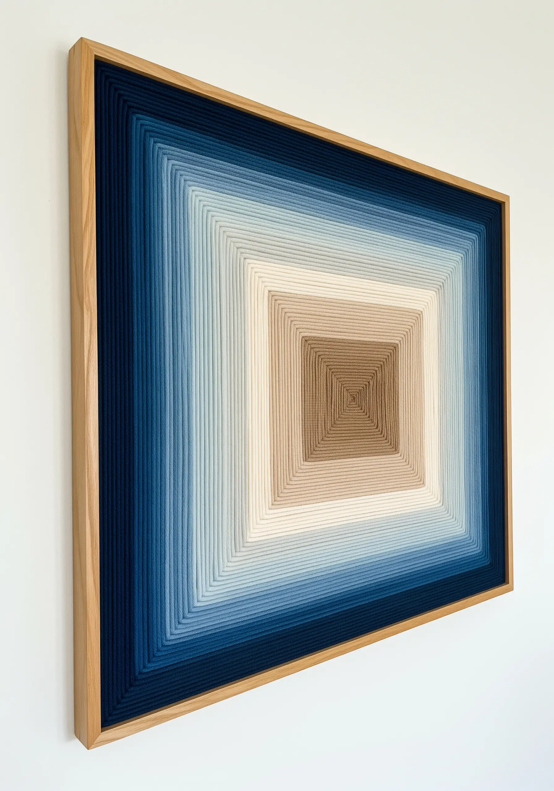 A rectangular wooden frame wrapped tightly with yarn in a gradient from dark blue to beige.