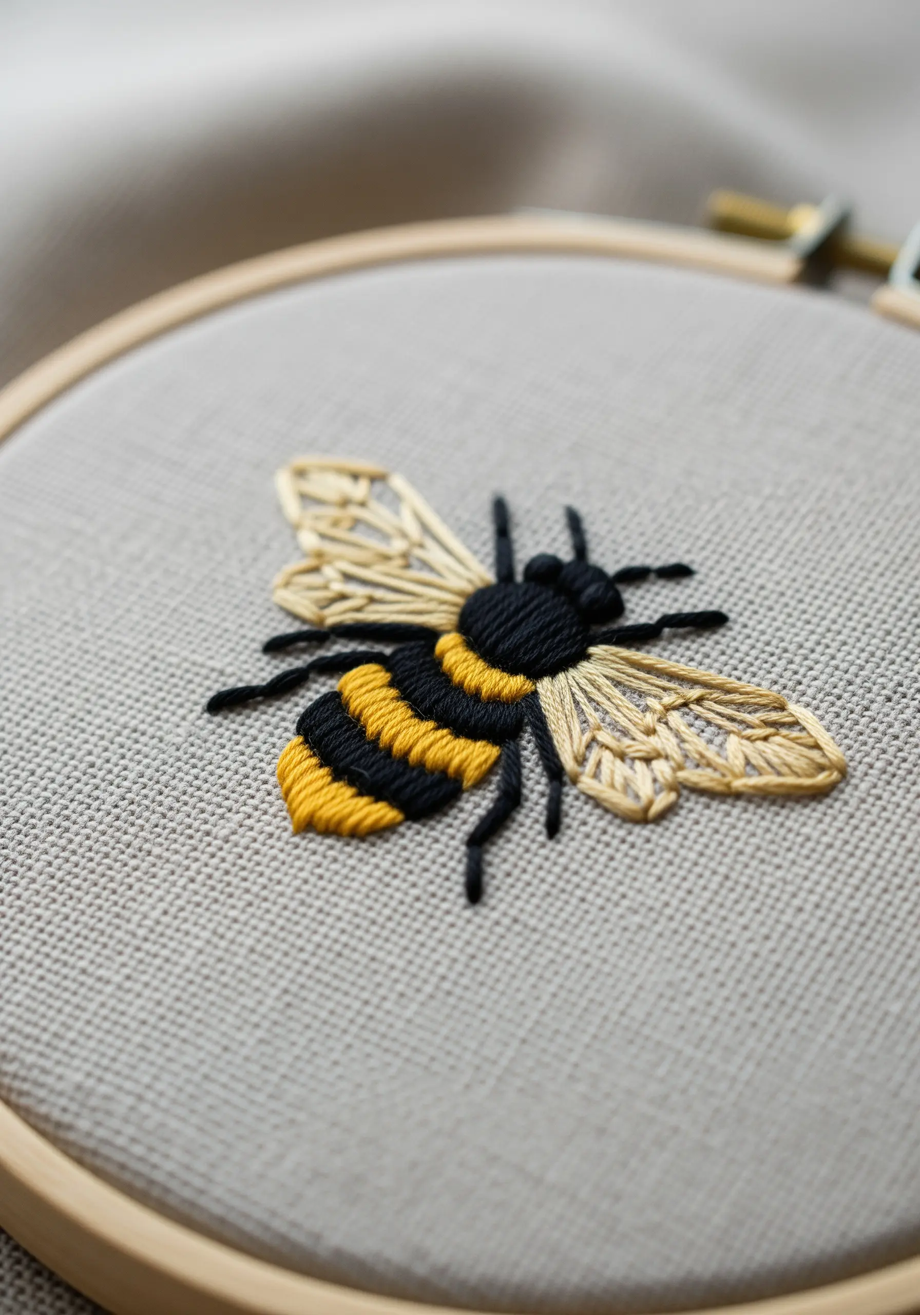 A realistic embroidered bee with detailed satin stitch body and translucent wings.