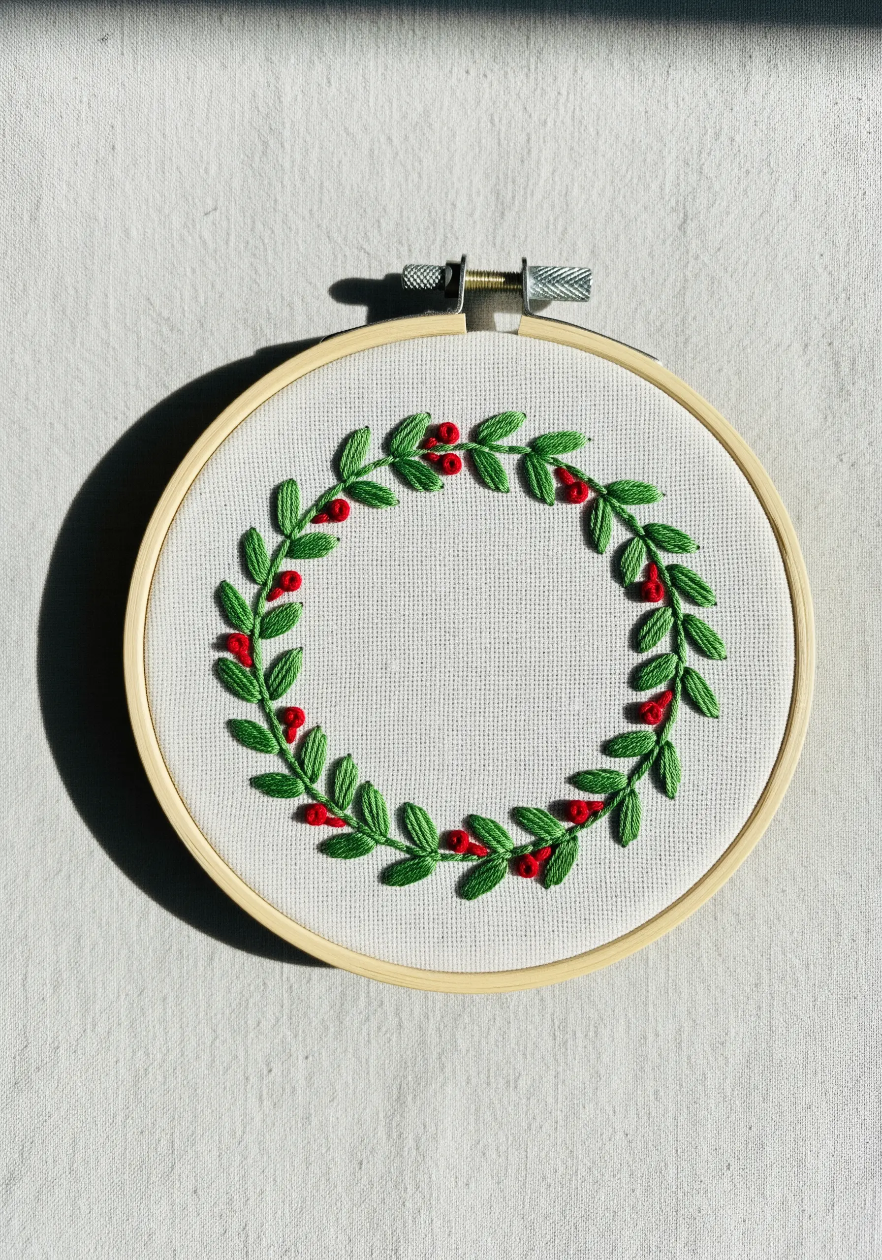 A festive wreath of green leaves and red berries embroidered in a hoop.