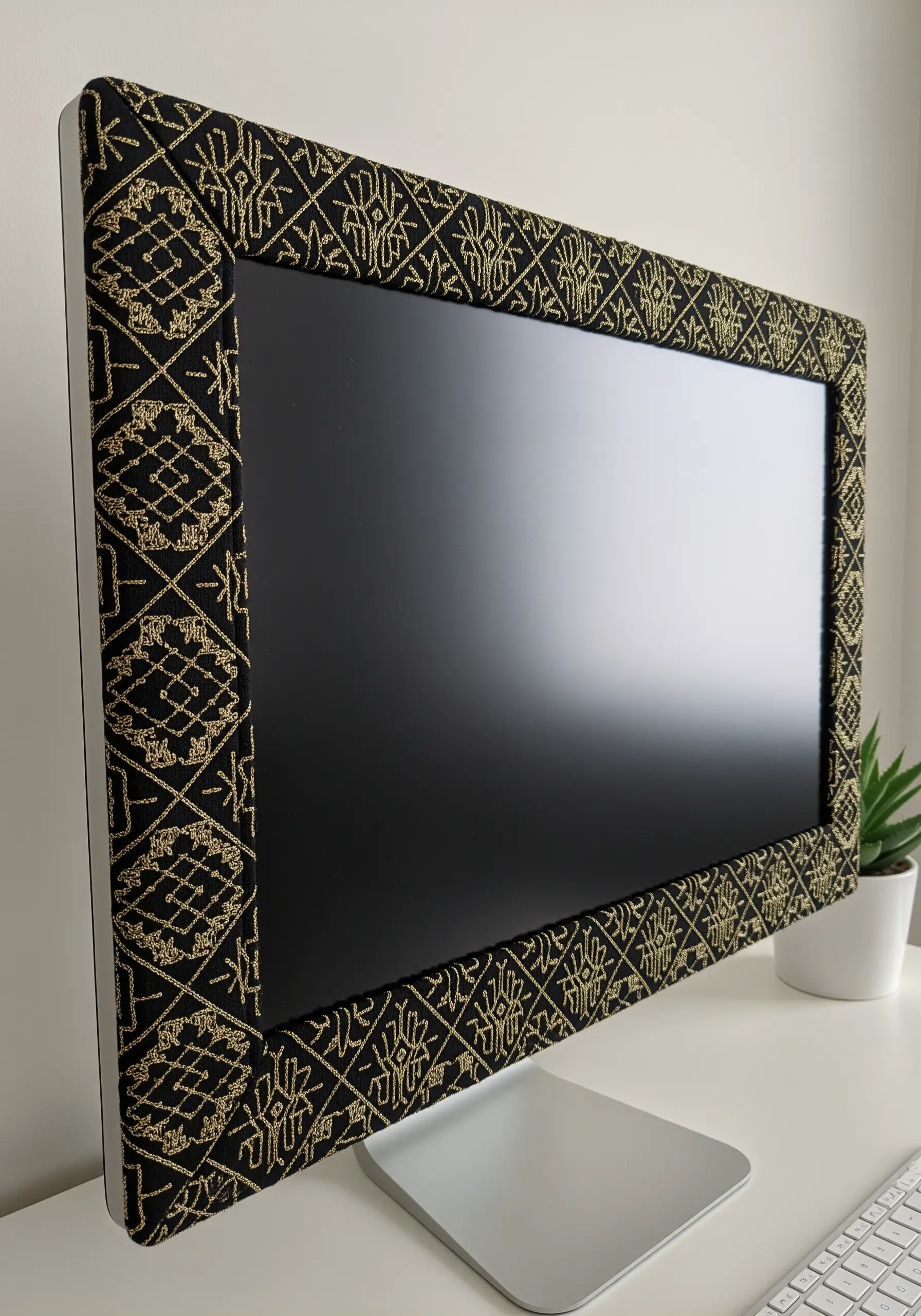 A computer monitor with its frame covered in a black fabric embroidered with a gold geometric pattern