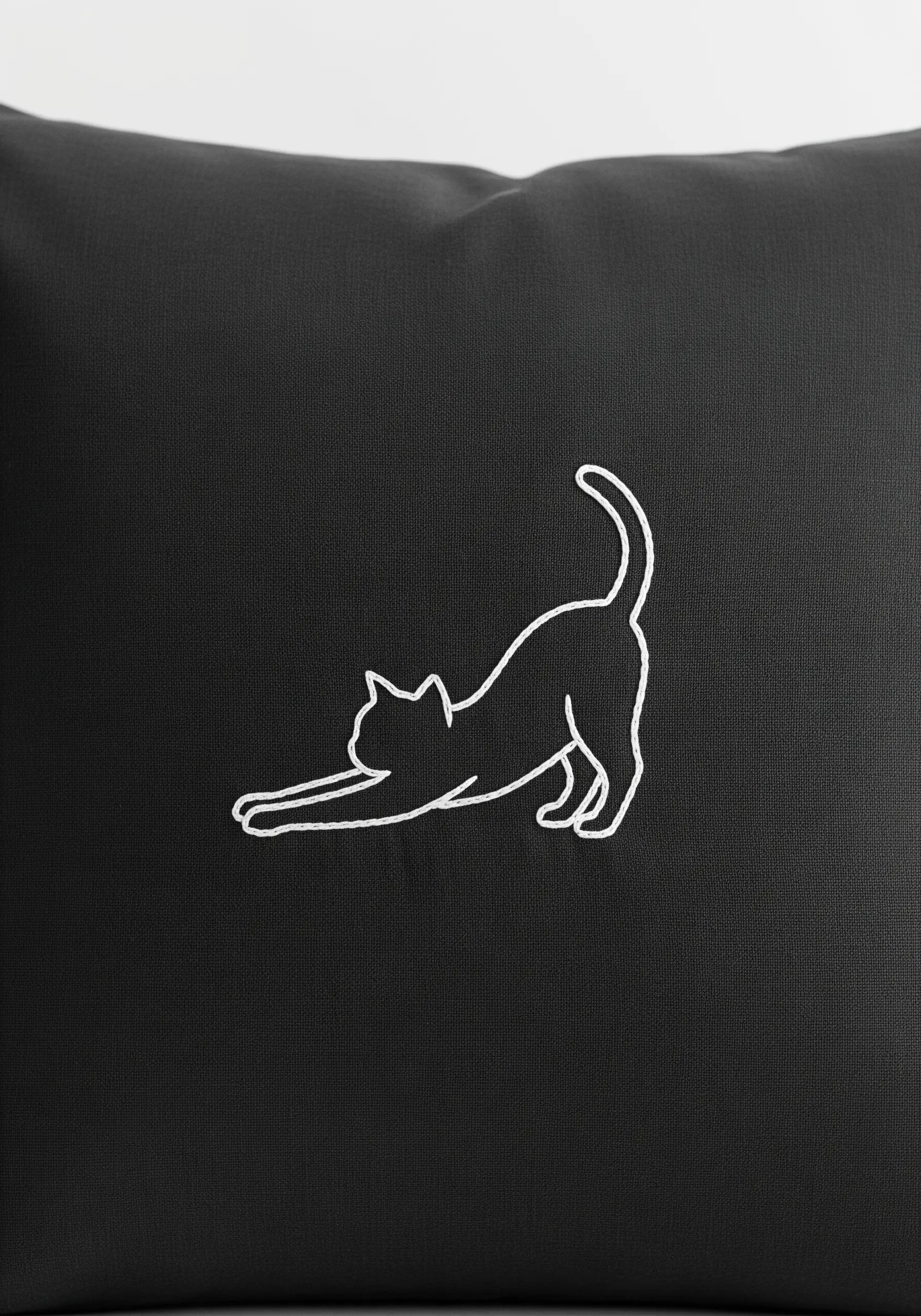 A minimalist white outline of a stretching cat embroidered on a black pillowcase.