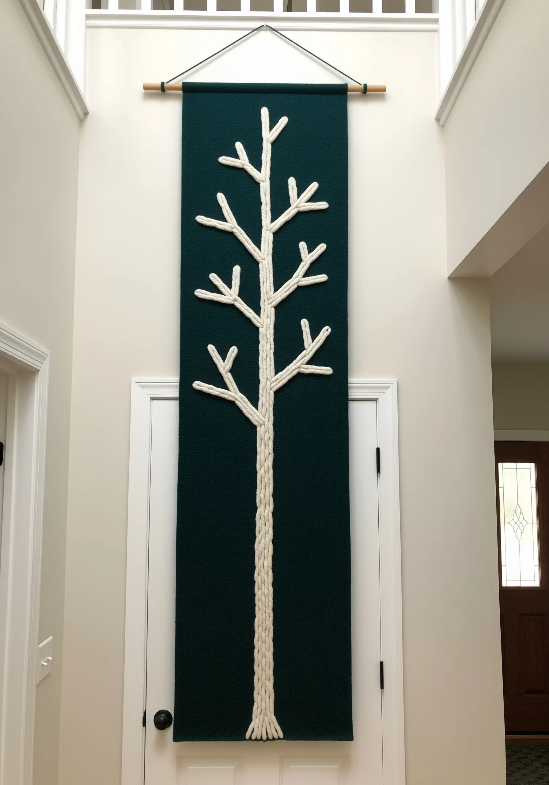 A large, dark green wall hanging with a minimalist tree silhouette made of thick white yarn.