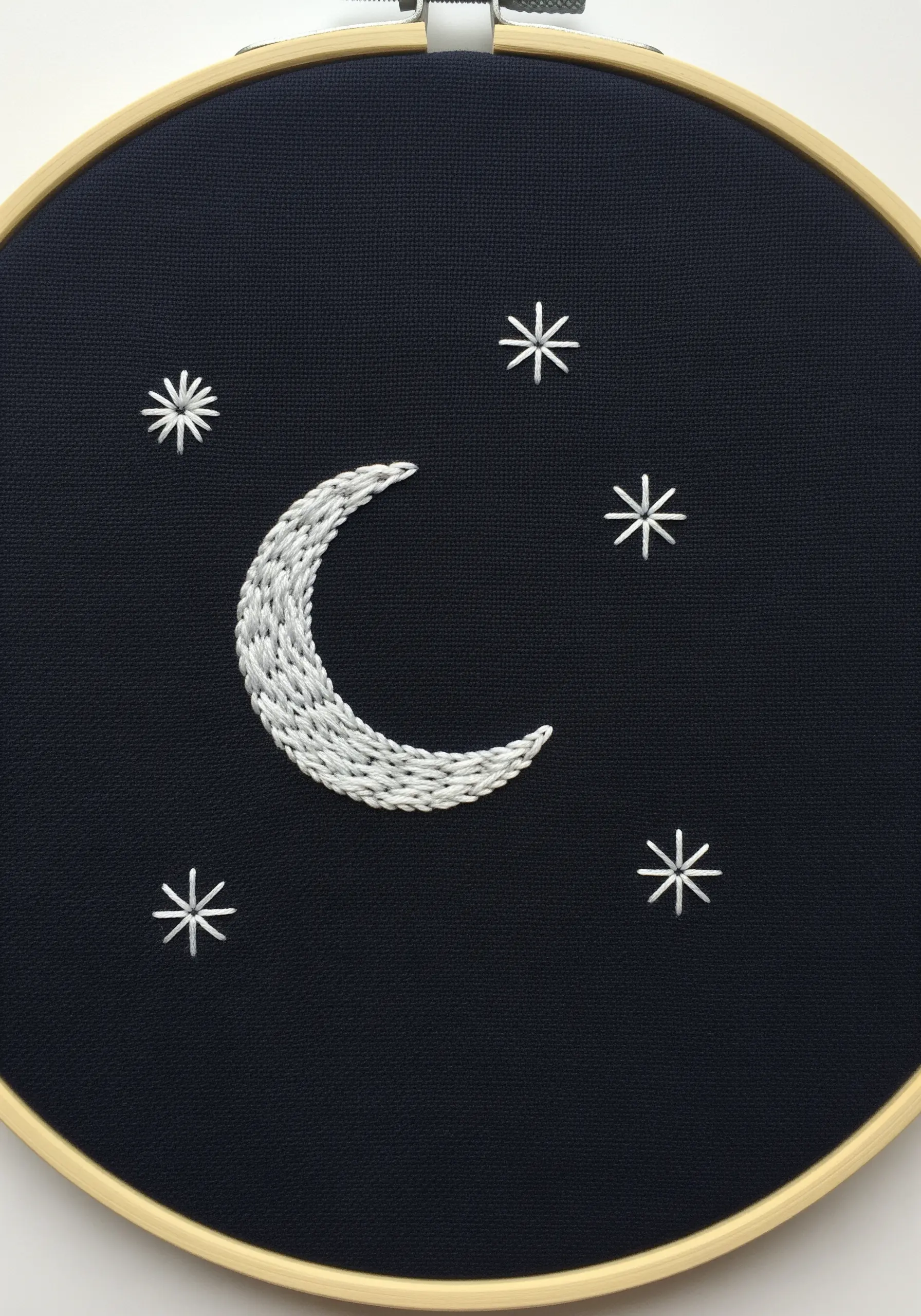 A crescent moon and stars embroidered in white thread on dark navy fabric.