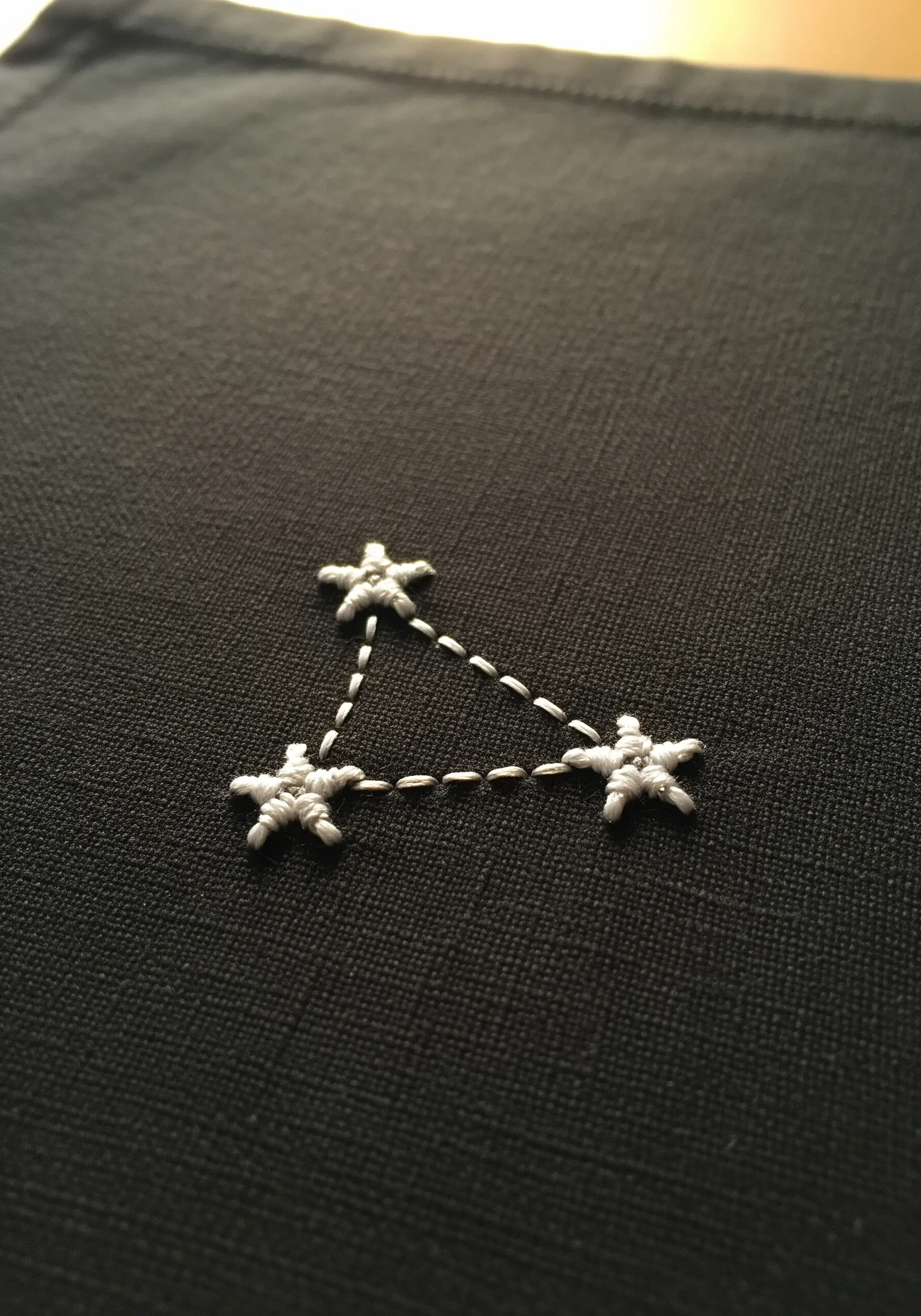 A tiny, three-star constellation stitched in white on black fabric.