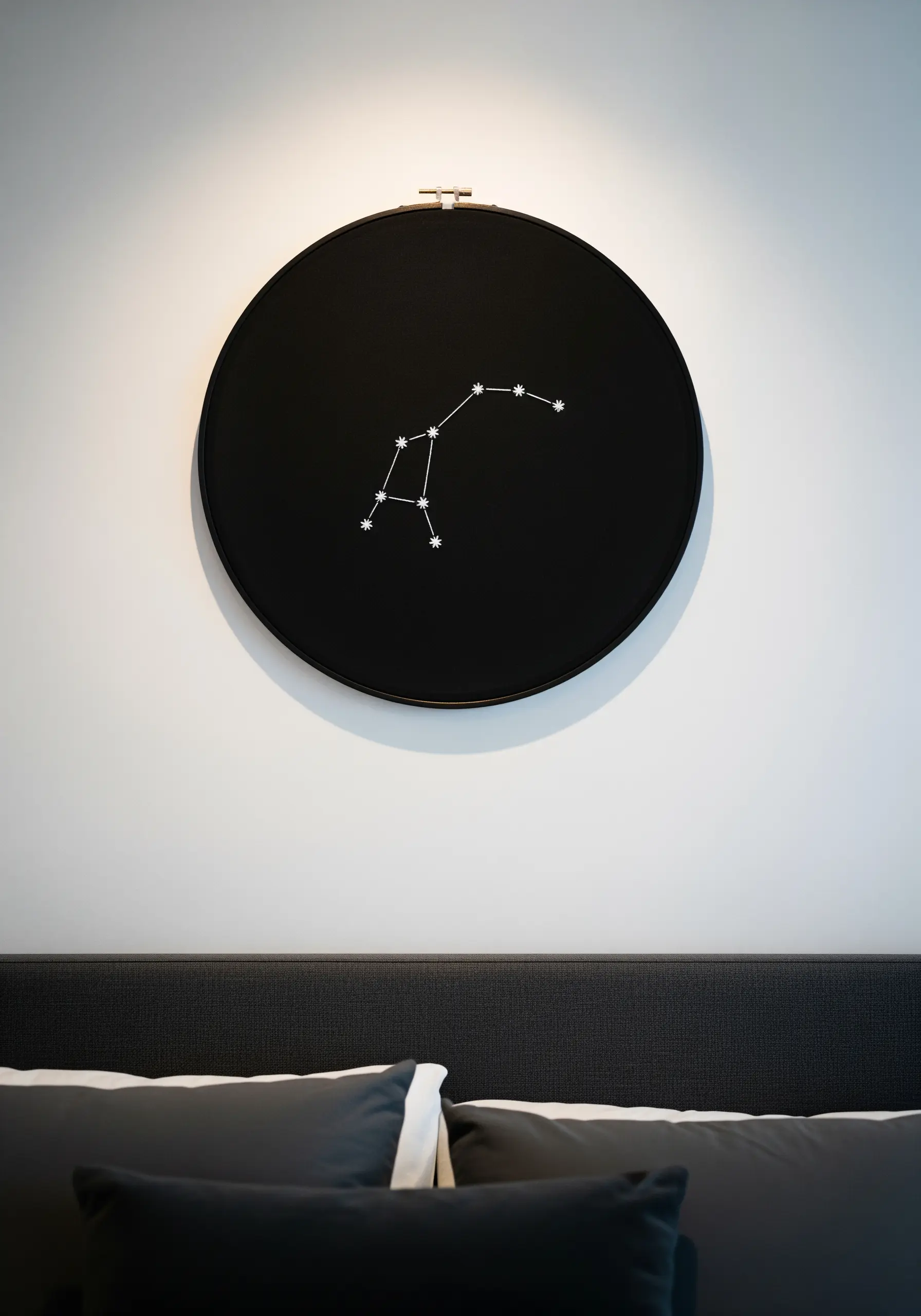The Big Dipper constellation stitched in white thread on black fabric in a hoop.