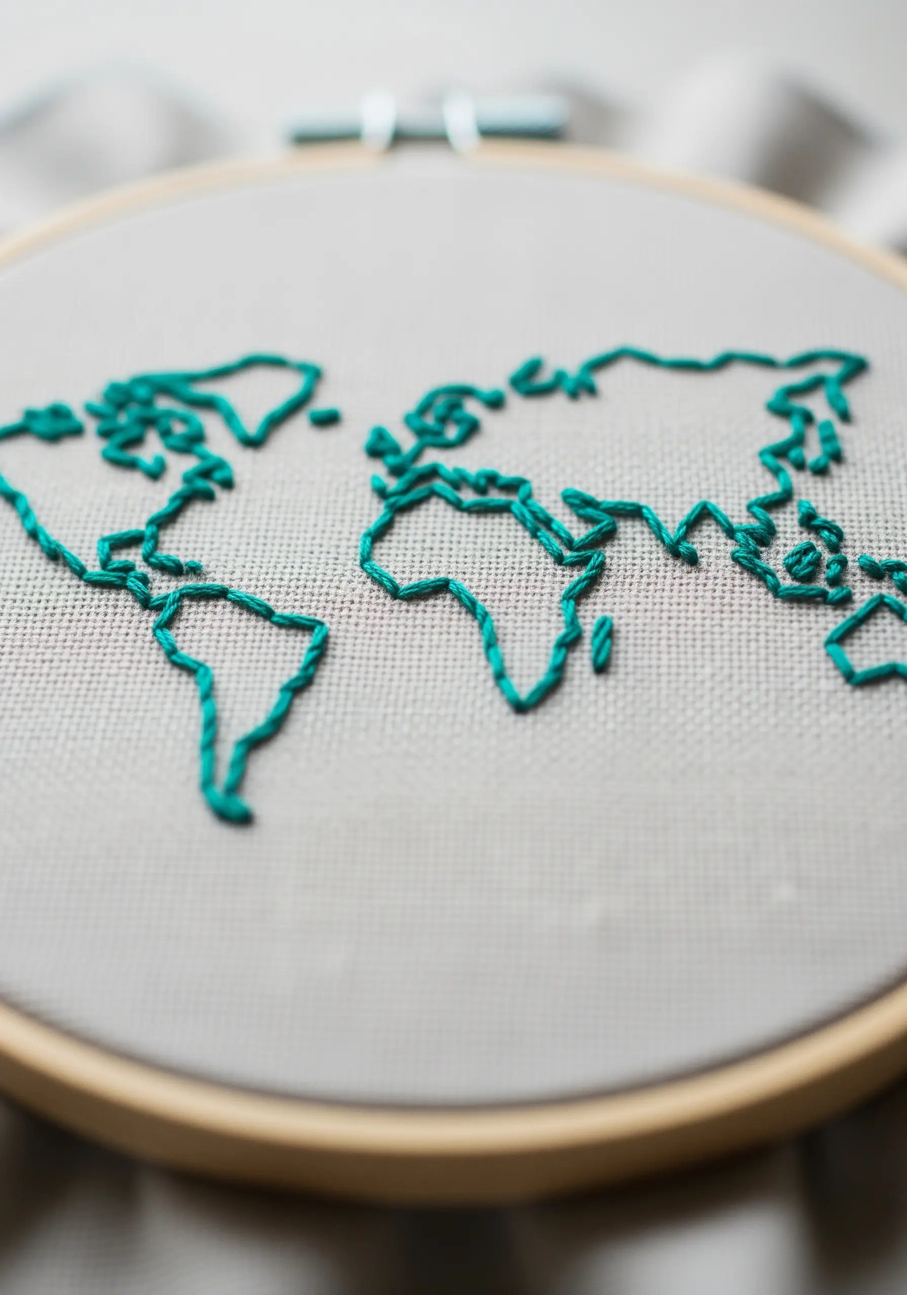 A world map outline stitched in teal thread on a neutral fabric background.