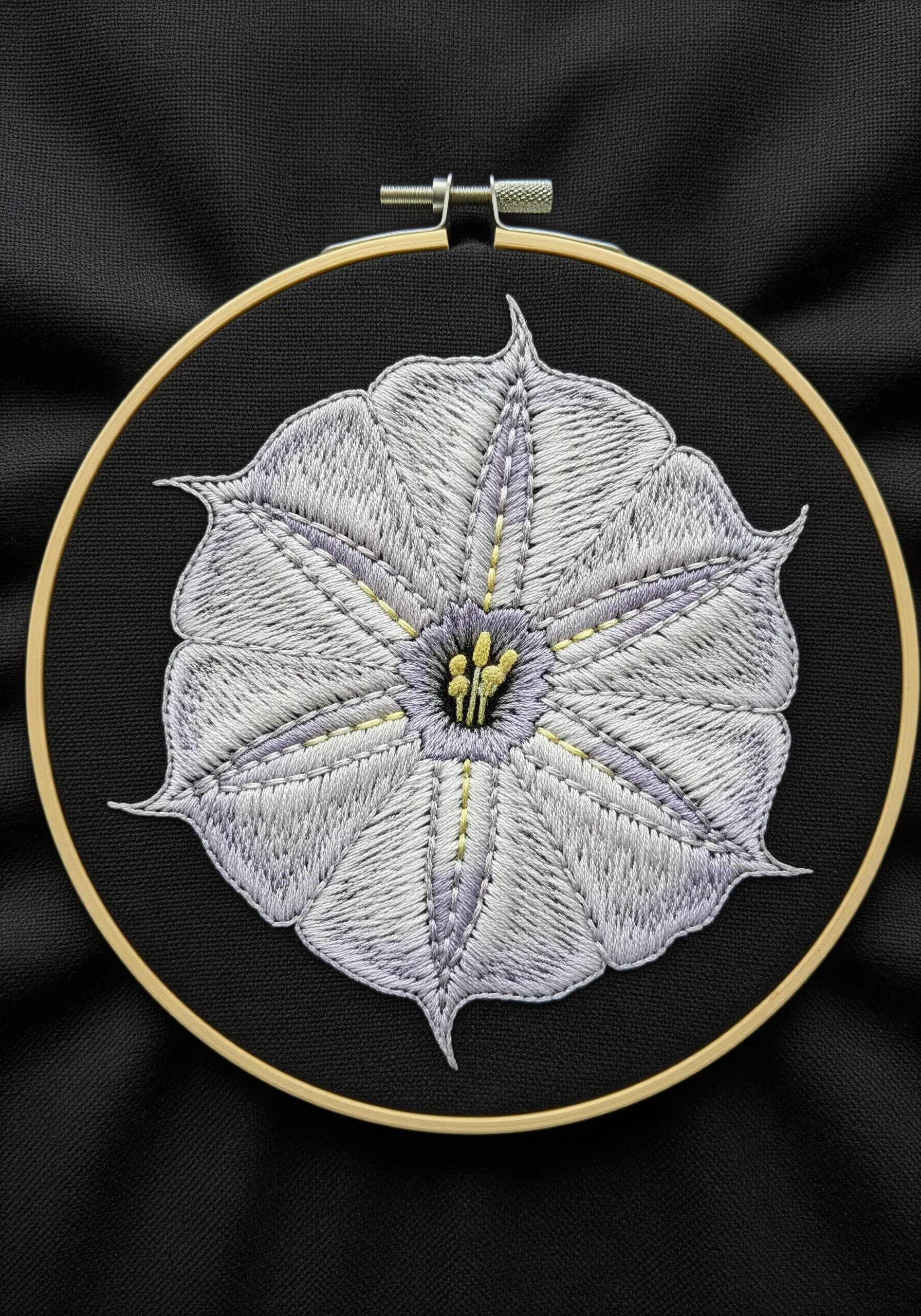 A symmetrical, top-down view of an embroidered white and lavender moonflower on black fabric.