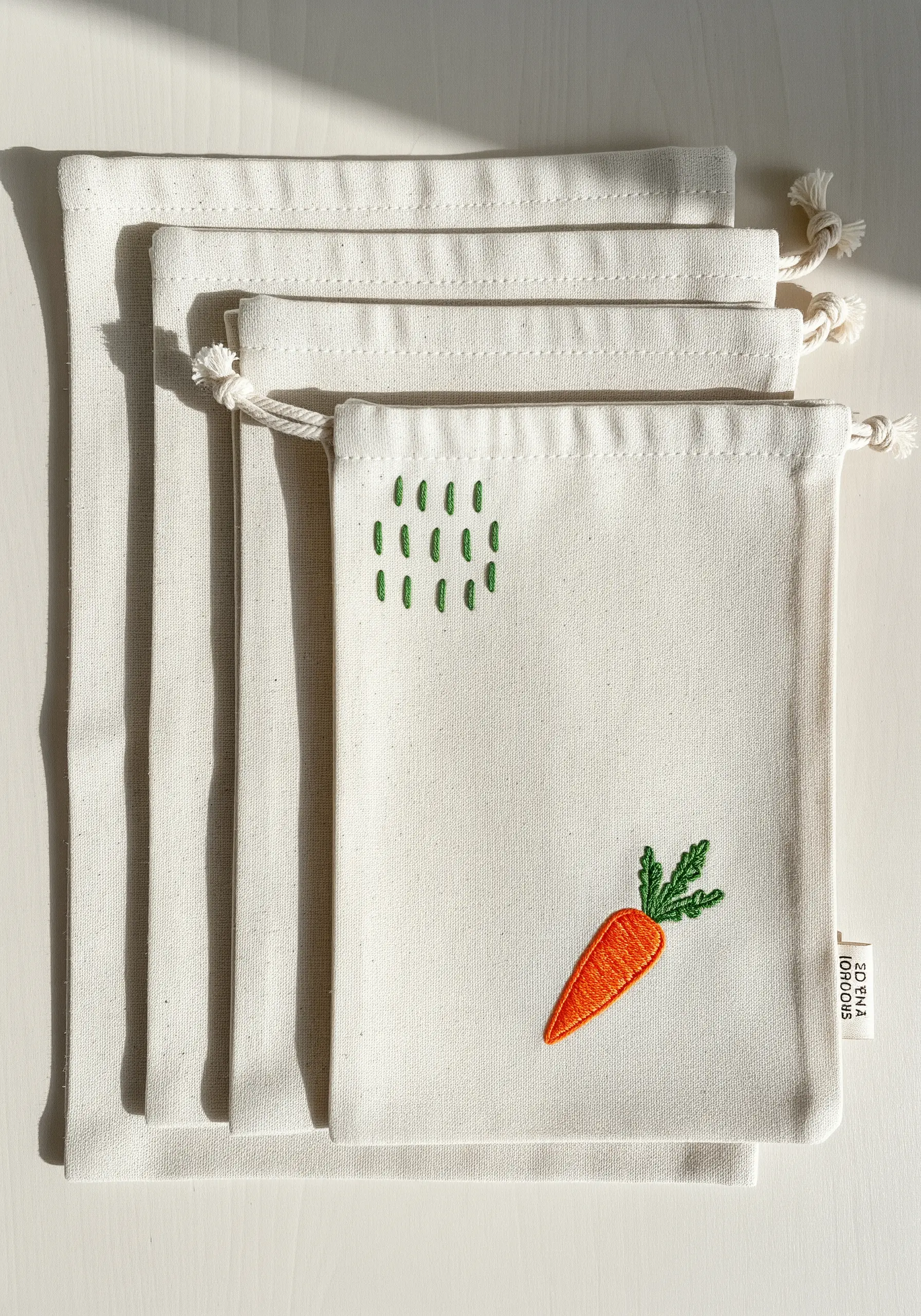 An embroidered carrot and abstract green dashes on canvas produce bags.