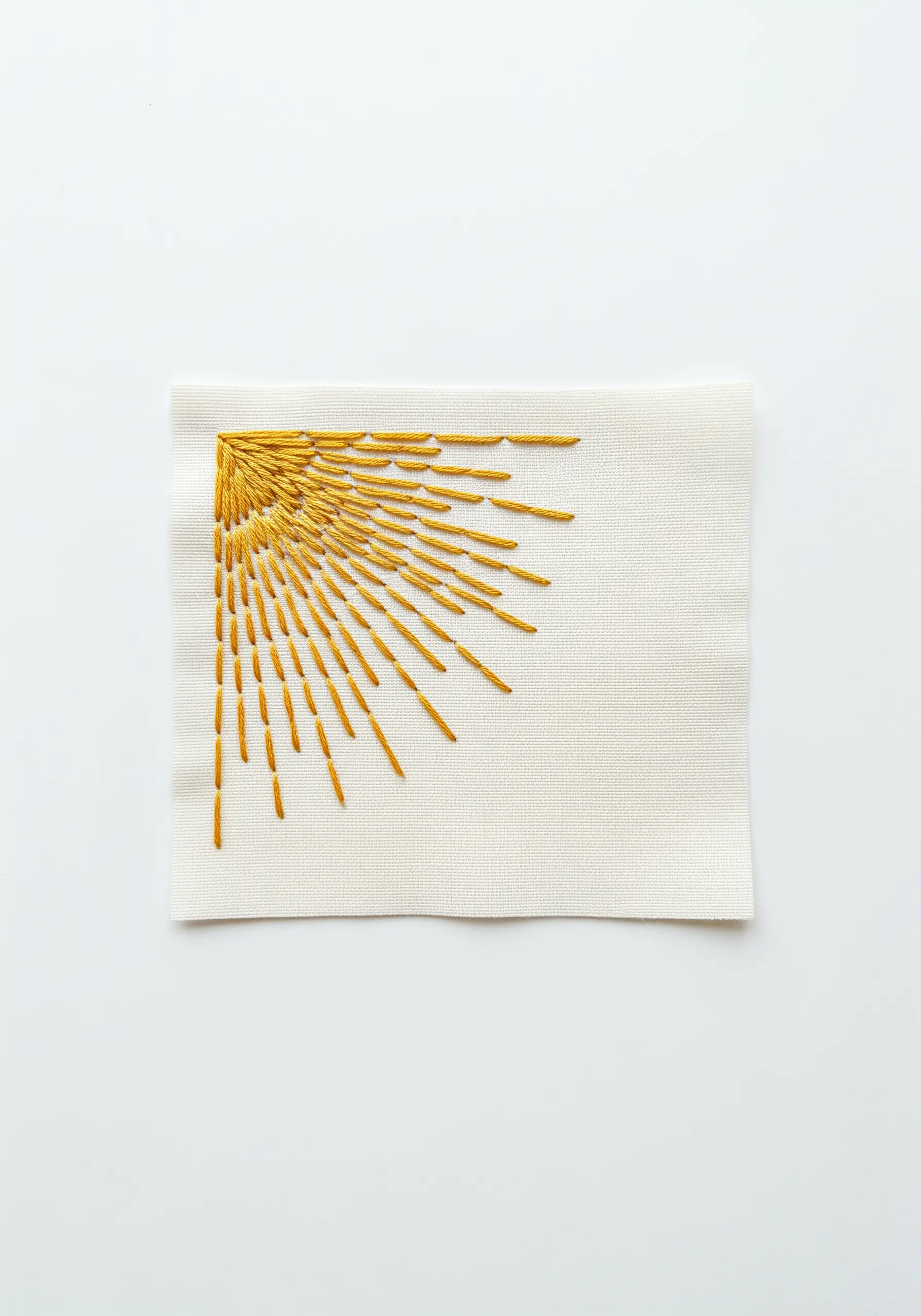 An embroidered sunburst in a corner, made with radiating yellow straight stitches.